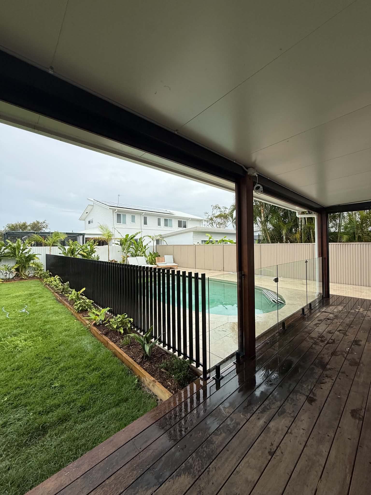 Covered patio overlooking a backyard pool, green lawn, and neighboring houses.