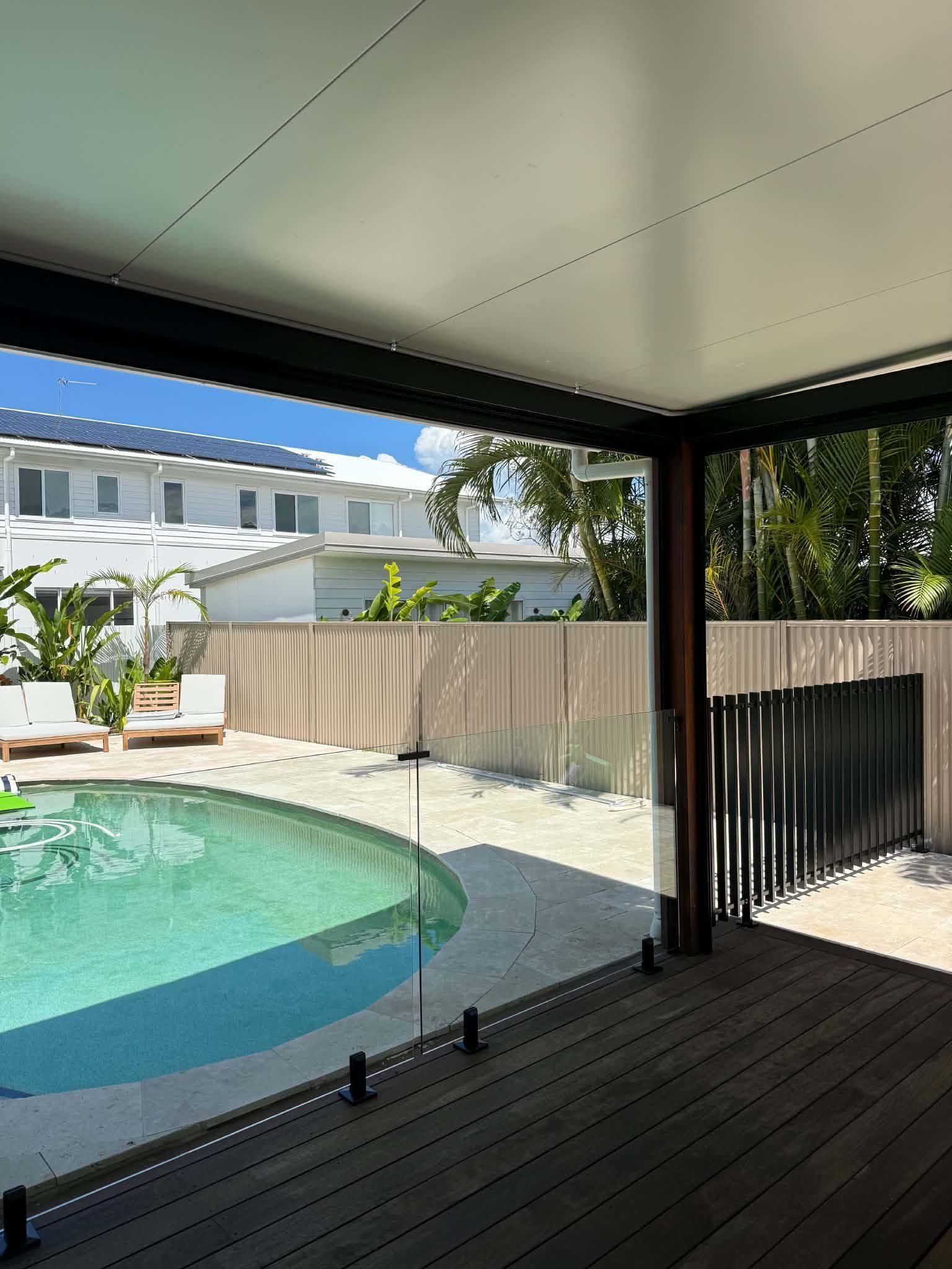 Covered patio beside turquoise pool with dark wood deck and beige privacy fence