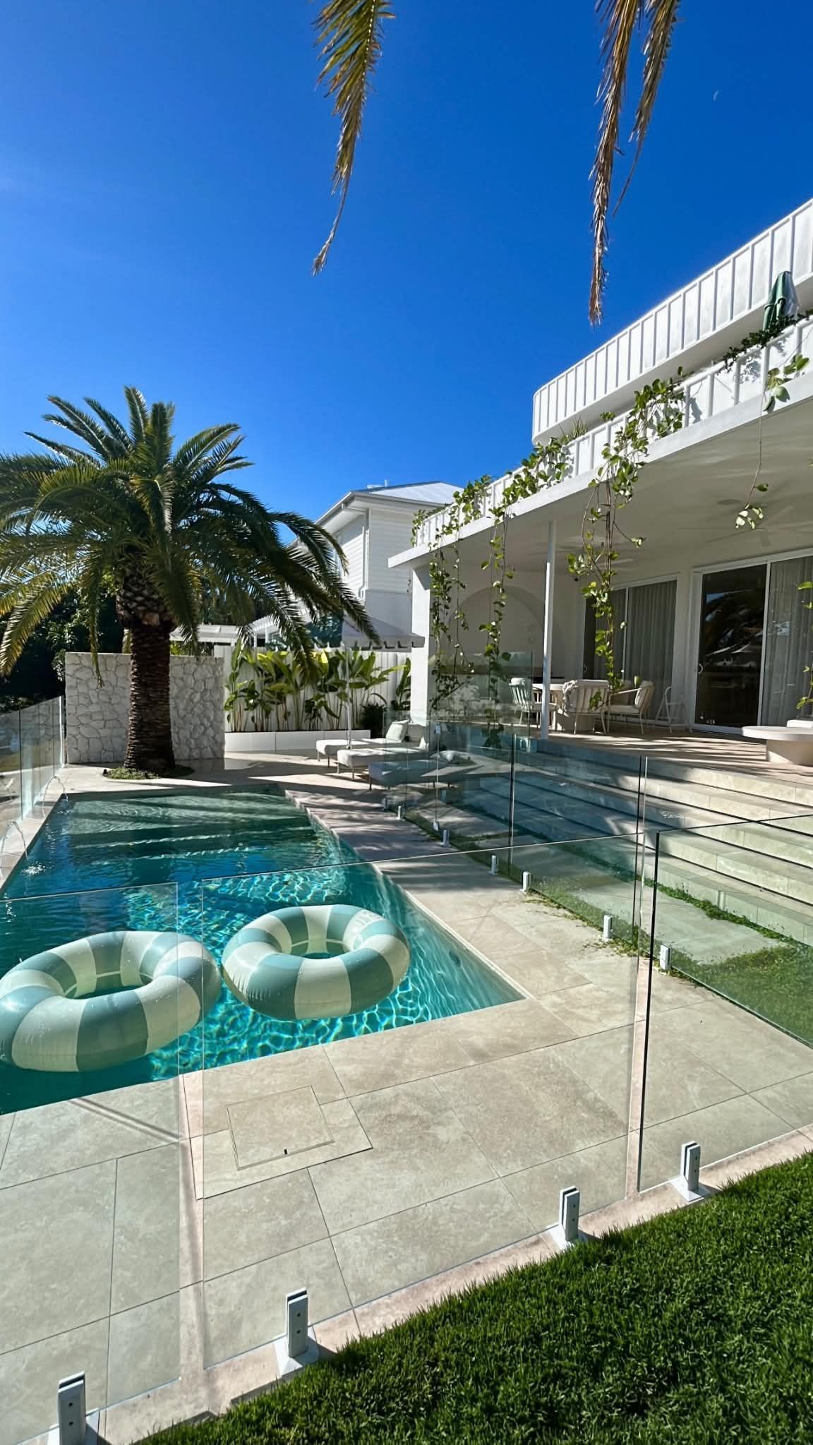 Modern villa courtyard with turquoise pool, white lounge chairs, and palm trees under a clear blue sky
