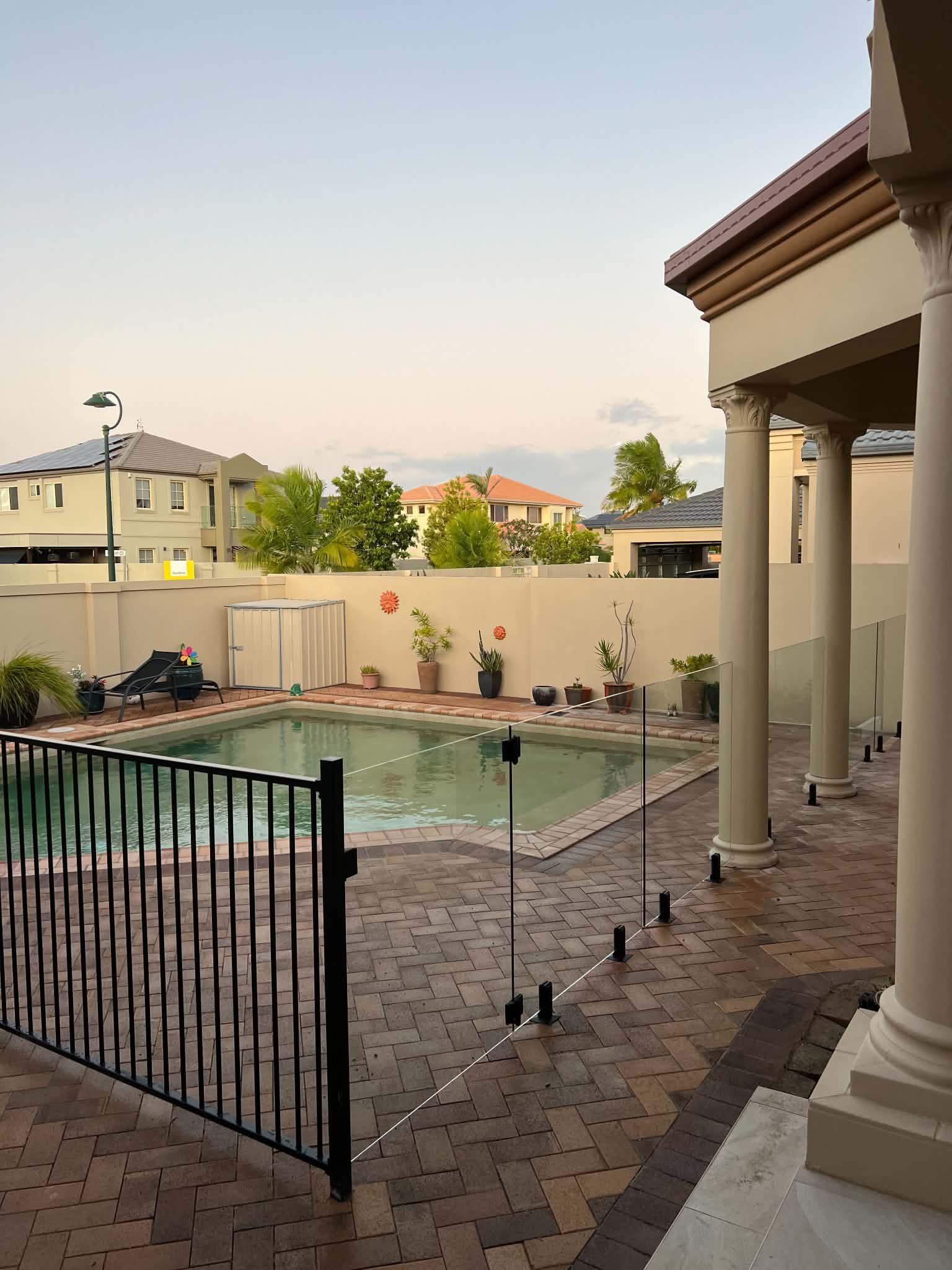 Backyard pool with tiled patio, black gate, and covered porch columns at sunset