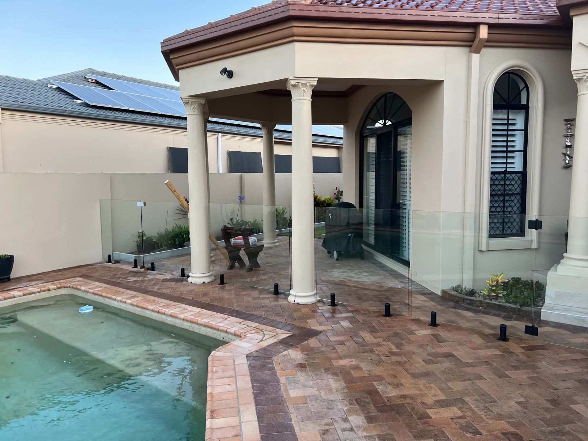 Backyard patio with a swimming pool, covered porch, columns, and a small dog by the walkway.