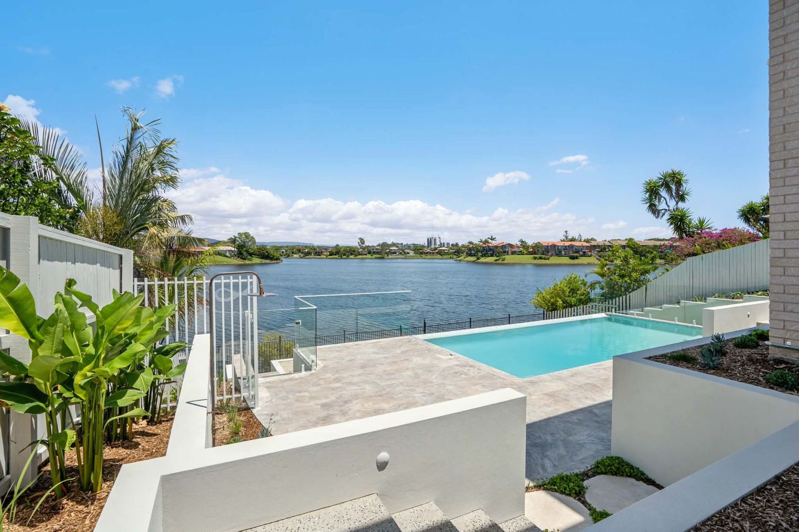 Modern patio with a turquoise pool overlooking a calm lake under a clear blue sky