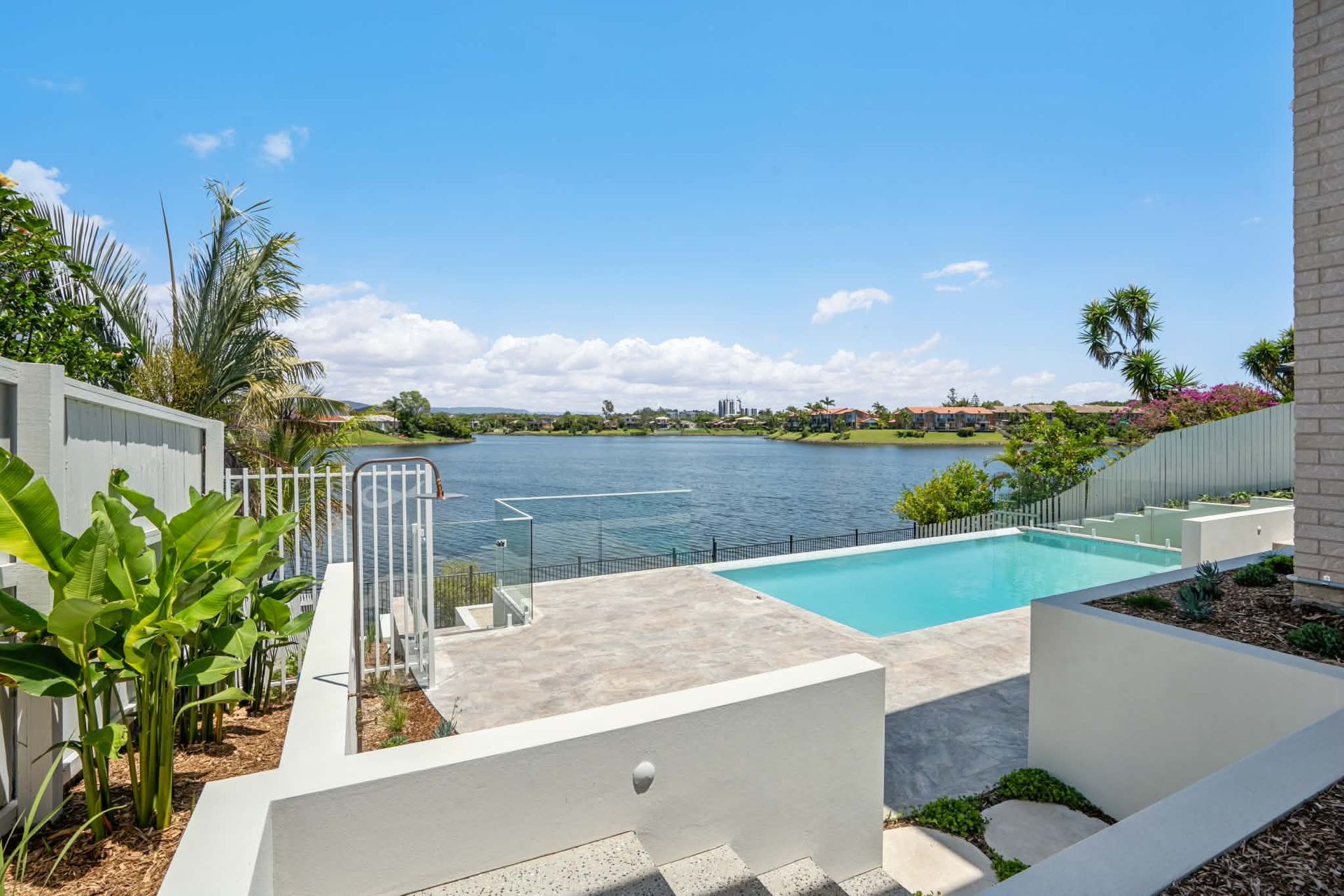 Modern patio with infinity pool overlooking a calm lake under a blue sky