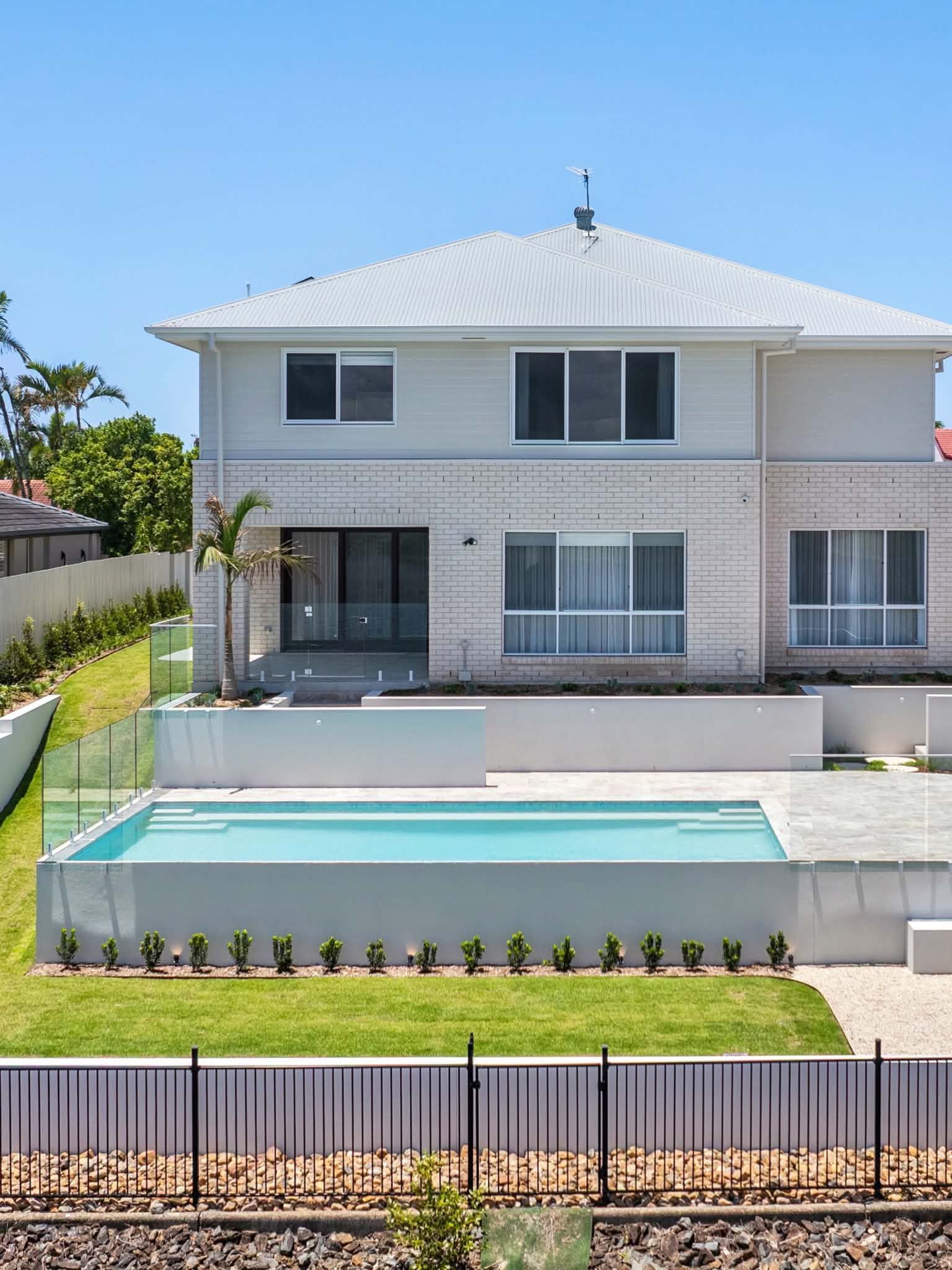 Modern two-story white house with a pool and fenced front yard under a bright blue sky