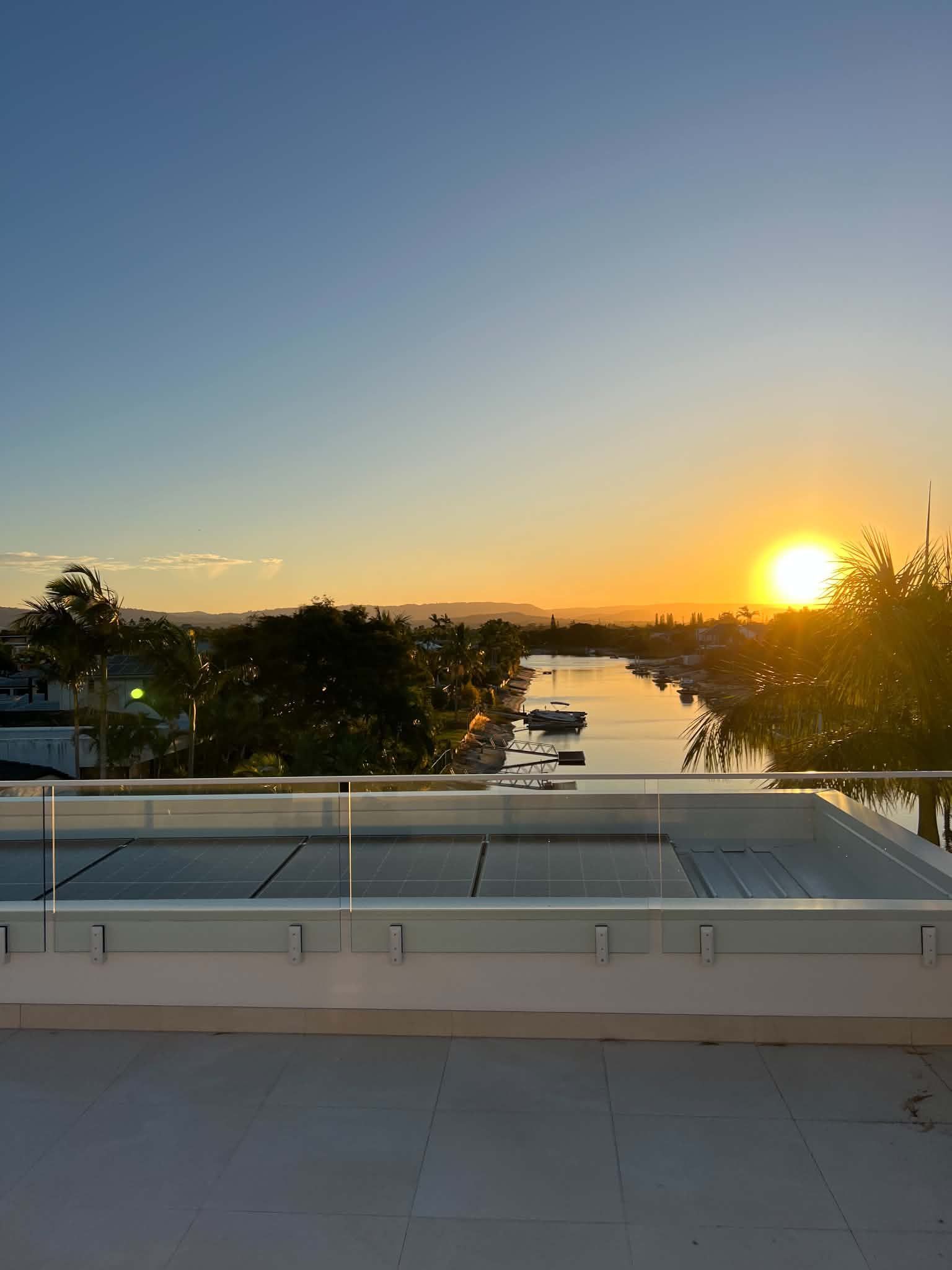 Sunset over a rooftop with trees and water in the distance, golden sky on the horizon