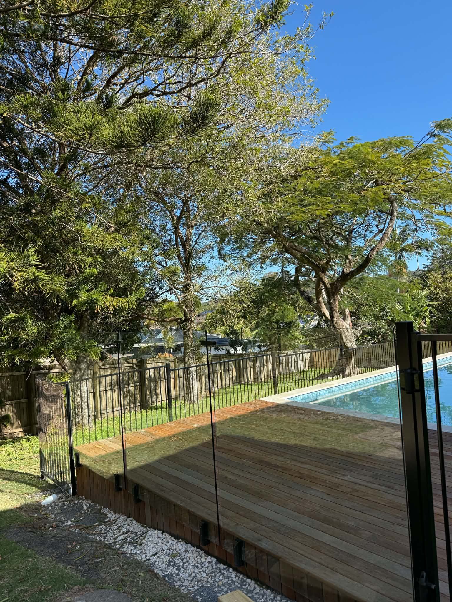 Wooden fence along a tree-lined path beside a blue-roofed structure under a sunny sky