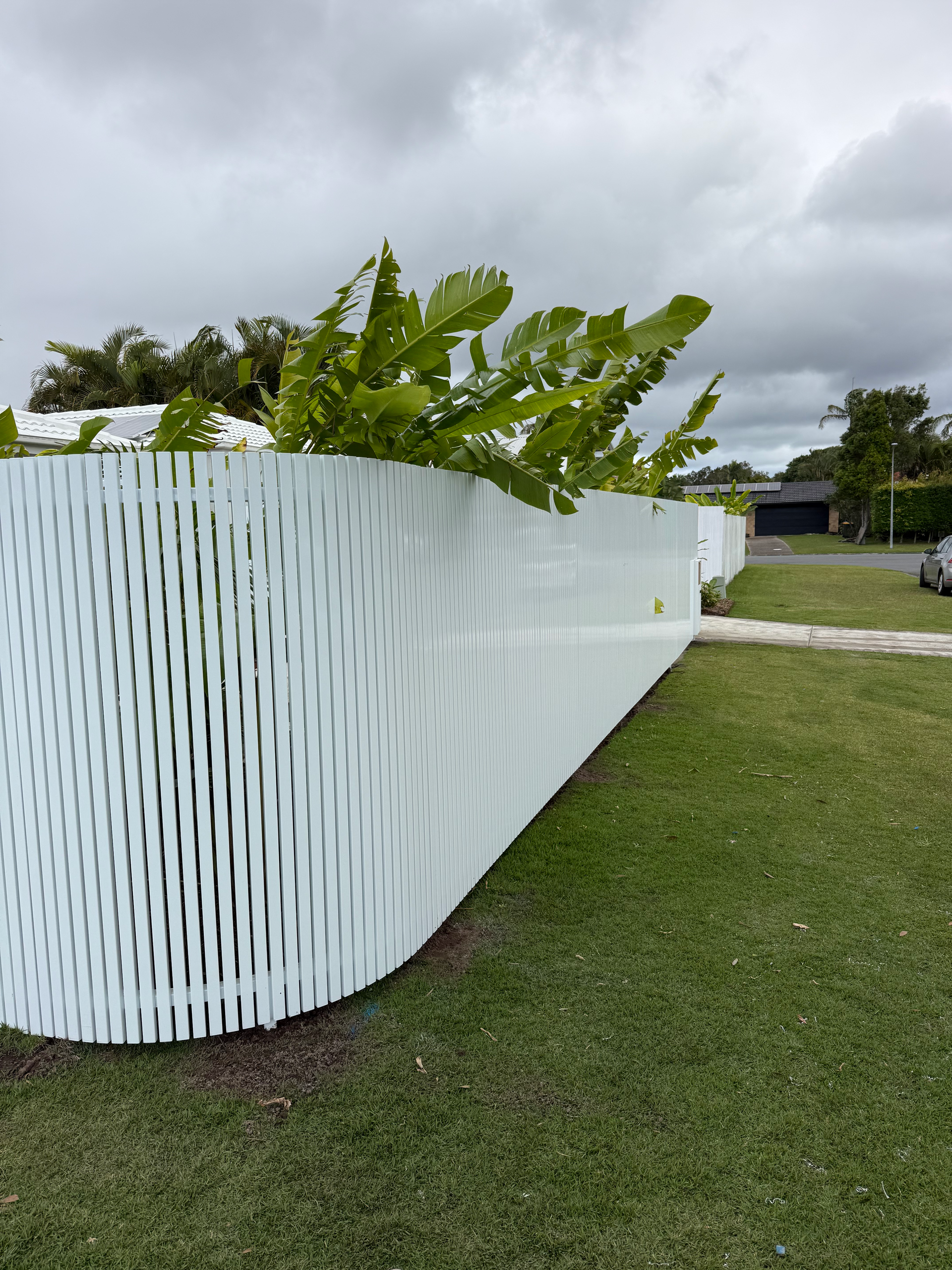 White curved planter with green plants beside a grassy field under a cloudy sky