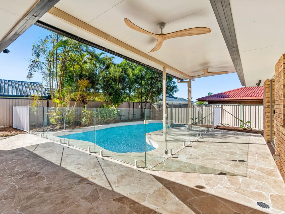 Covered patio overlooking a blue swimming pool and backyard with trees and fencing