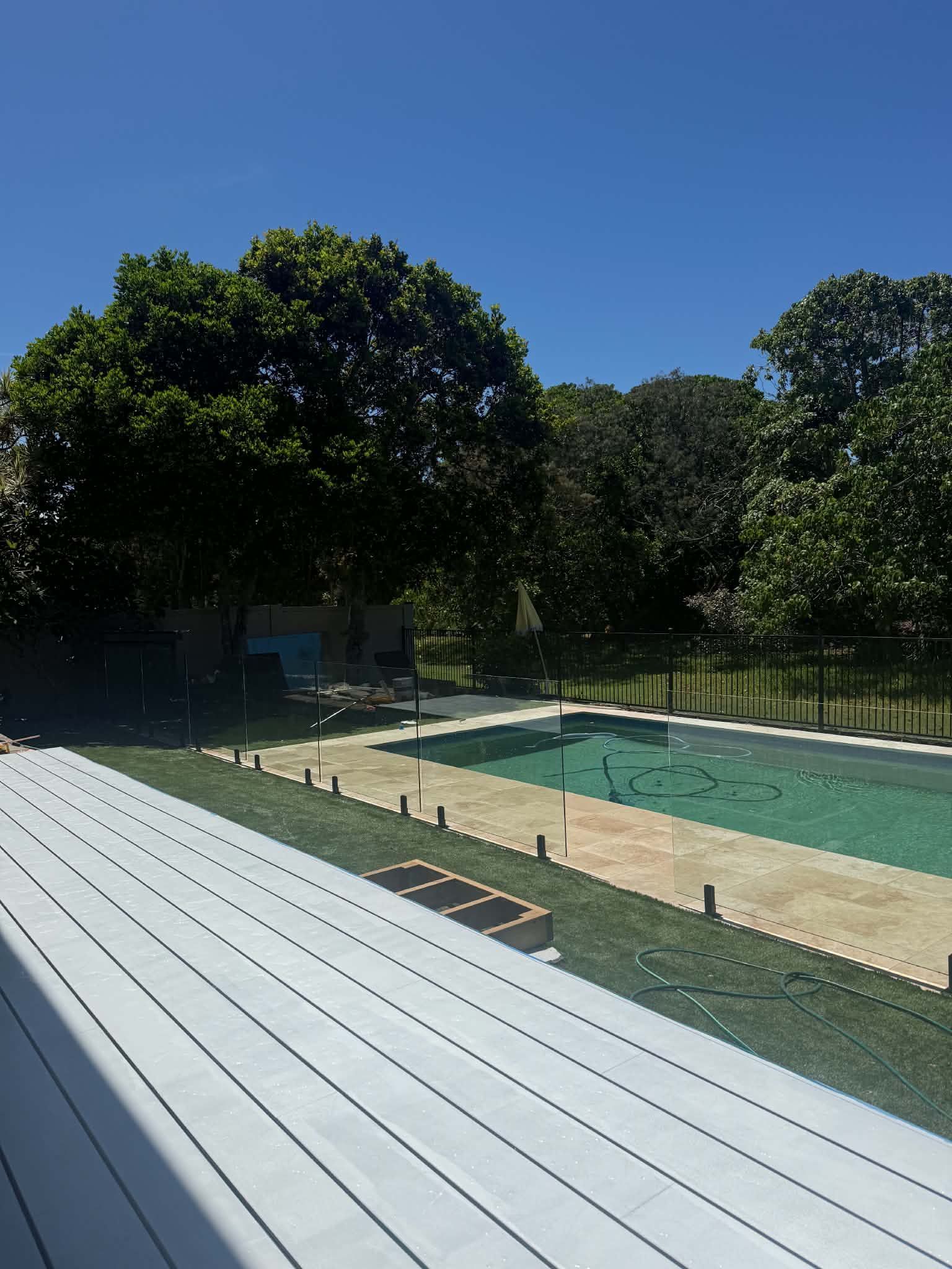 Outdoor swimming pool with pale blue water, white deck benches, and trees casting shade nearby