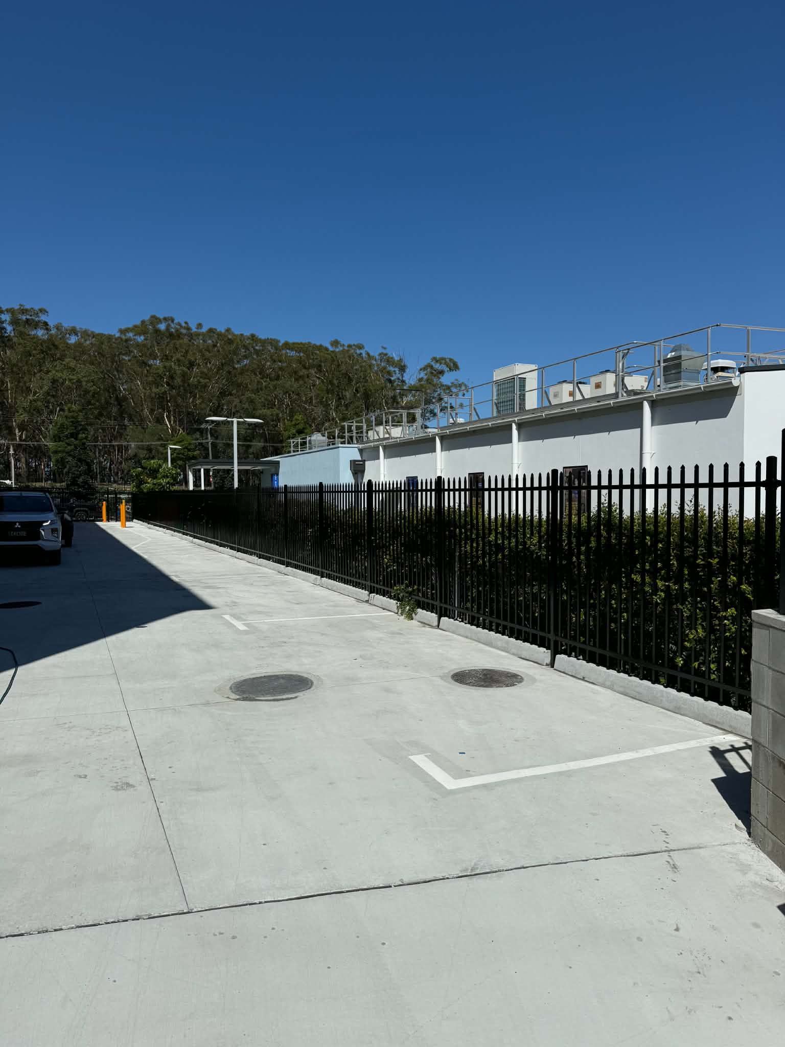 Sidewalk beside a black fence and white building under a clear blue sky