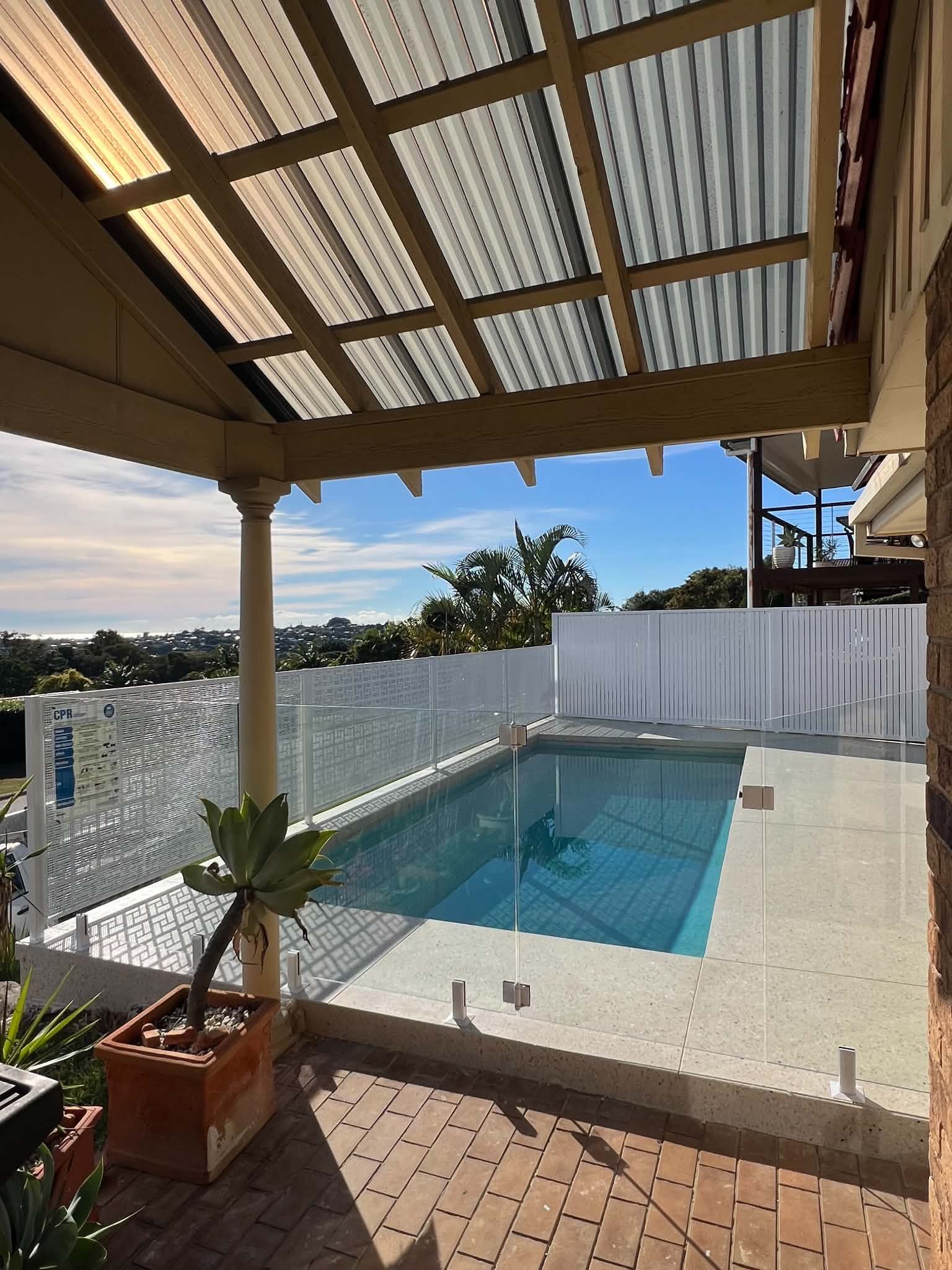 Covered backyard patio with a small rectangular pool, white walls, and blue sky beyond.