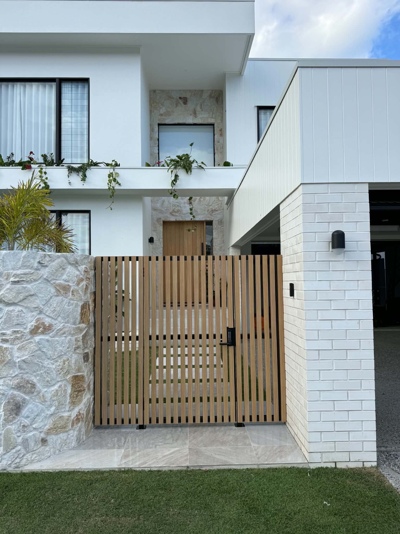 Modern white house with wooden gate, stone wall, and small front lawn