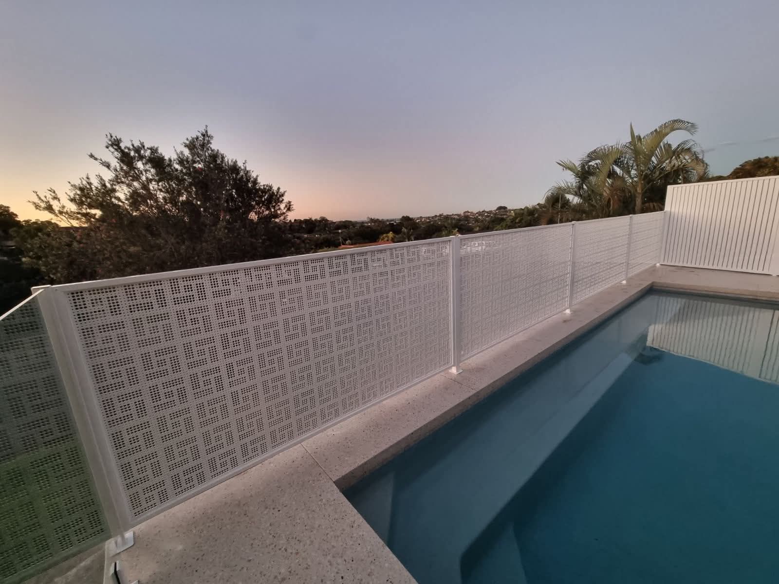 Poolside view with white lattice fence at sunset, overlooking trees and a blue swimming pool