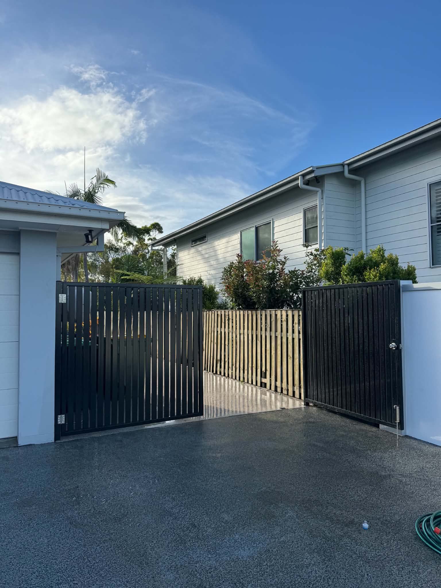 Driveway with dark wooden gates, white house walls, and a blue sky with wispy clouds.