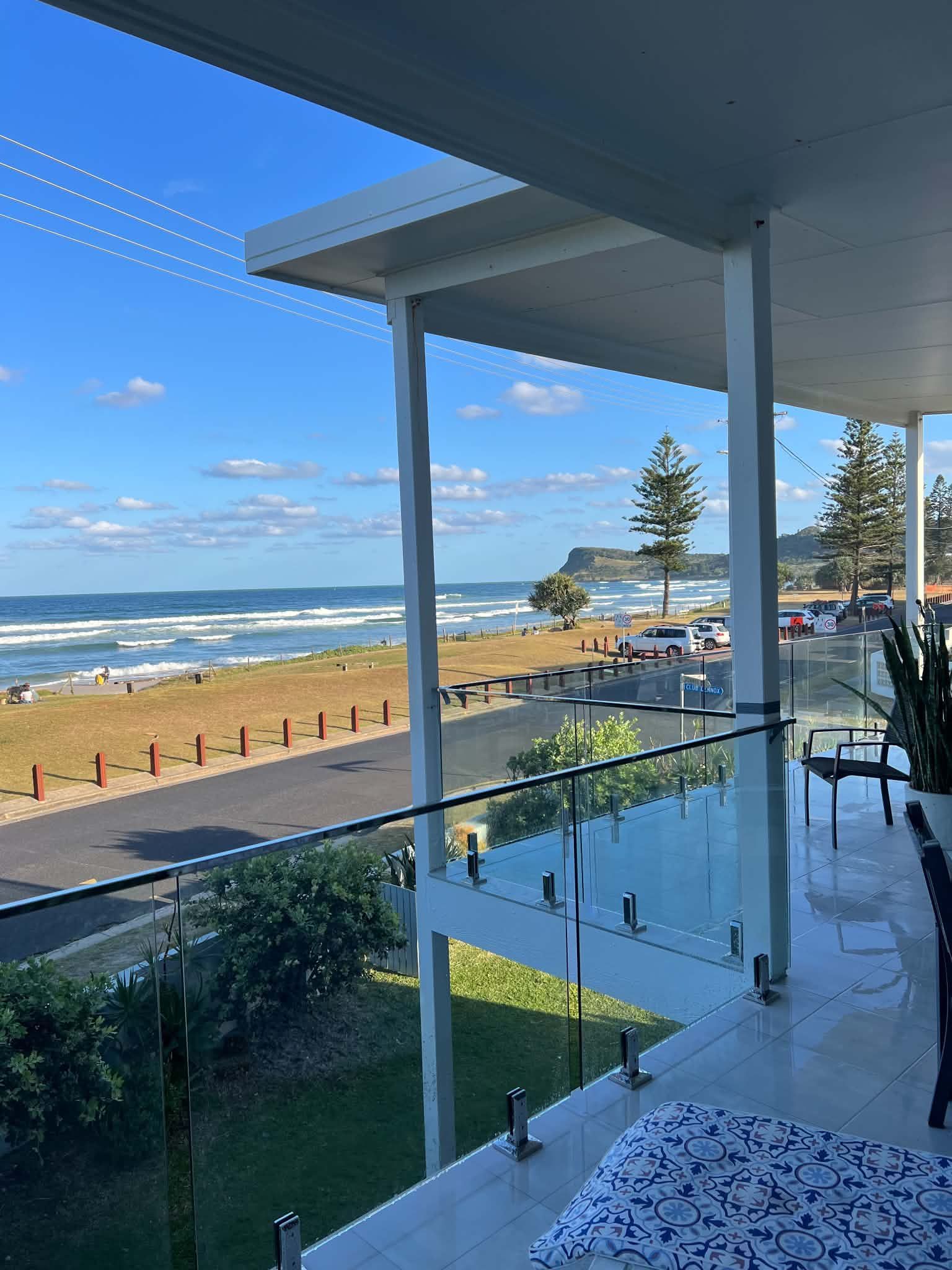 Beachfront balcony overlooking ocean, sandy shore, and blue sky on a sunny day.
