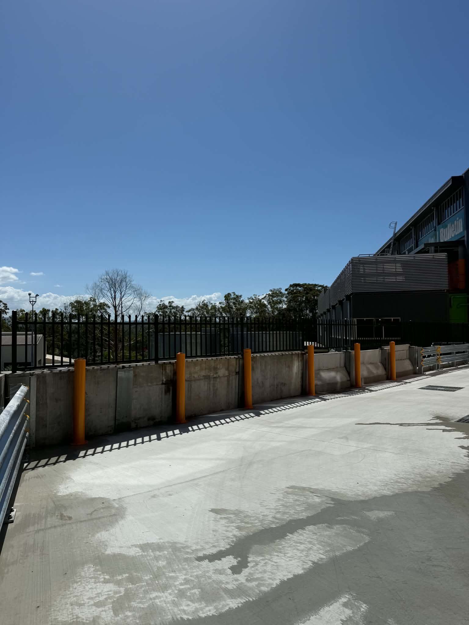 Concrete yard beside a black fence and house under a clear blue sky
