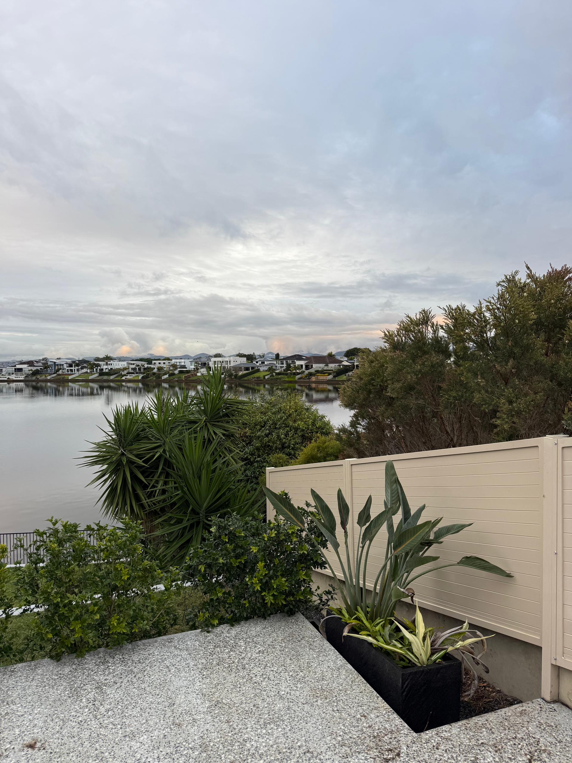 Lake view from a patio with potted plants, gravel ground, and a cloudy sky