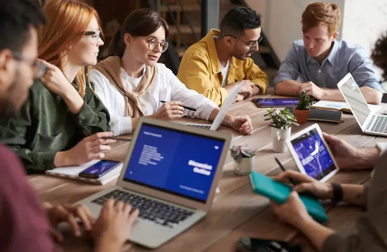 Group of people collaborating around a table with laptops and notebooks in a meeting room