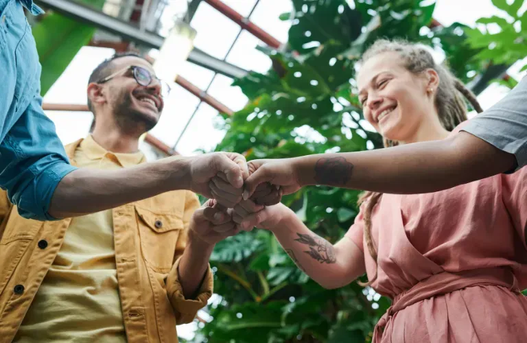Three people smiling and shaking hands in a greenhouse with lush green plants