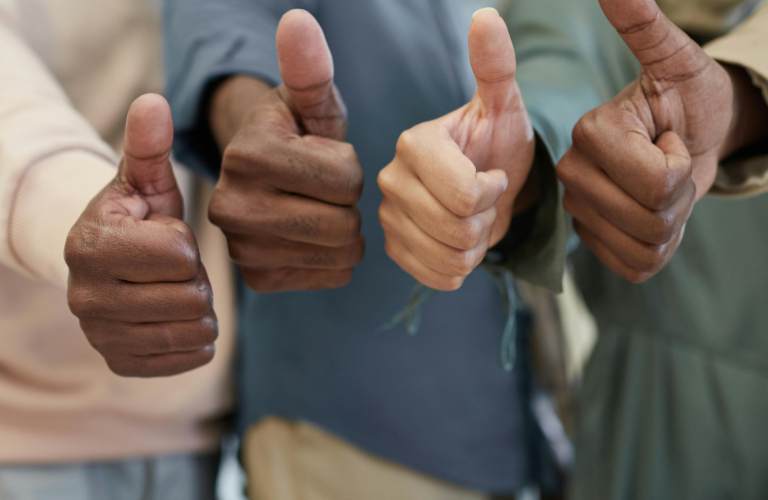 Several people hold up thumbs-up gestures against a blurred background.