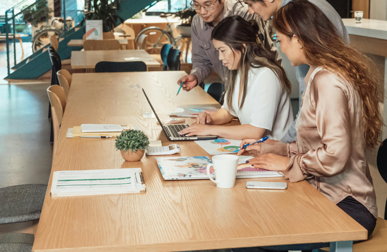 People working on laptops at a long wooden table in a bright office or café