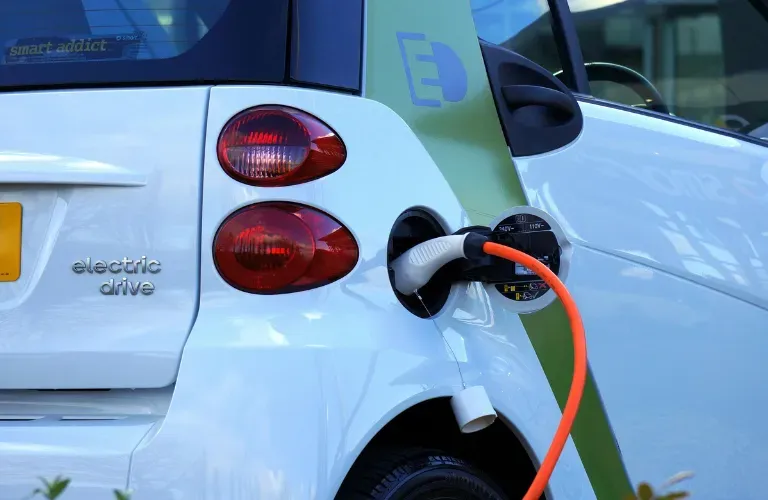 White electric car charging at a station with an orange cable connected to the rear side port