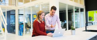 Two coworkers collaborating at a laptop in a bright office lounge