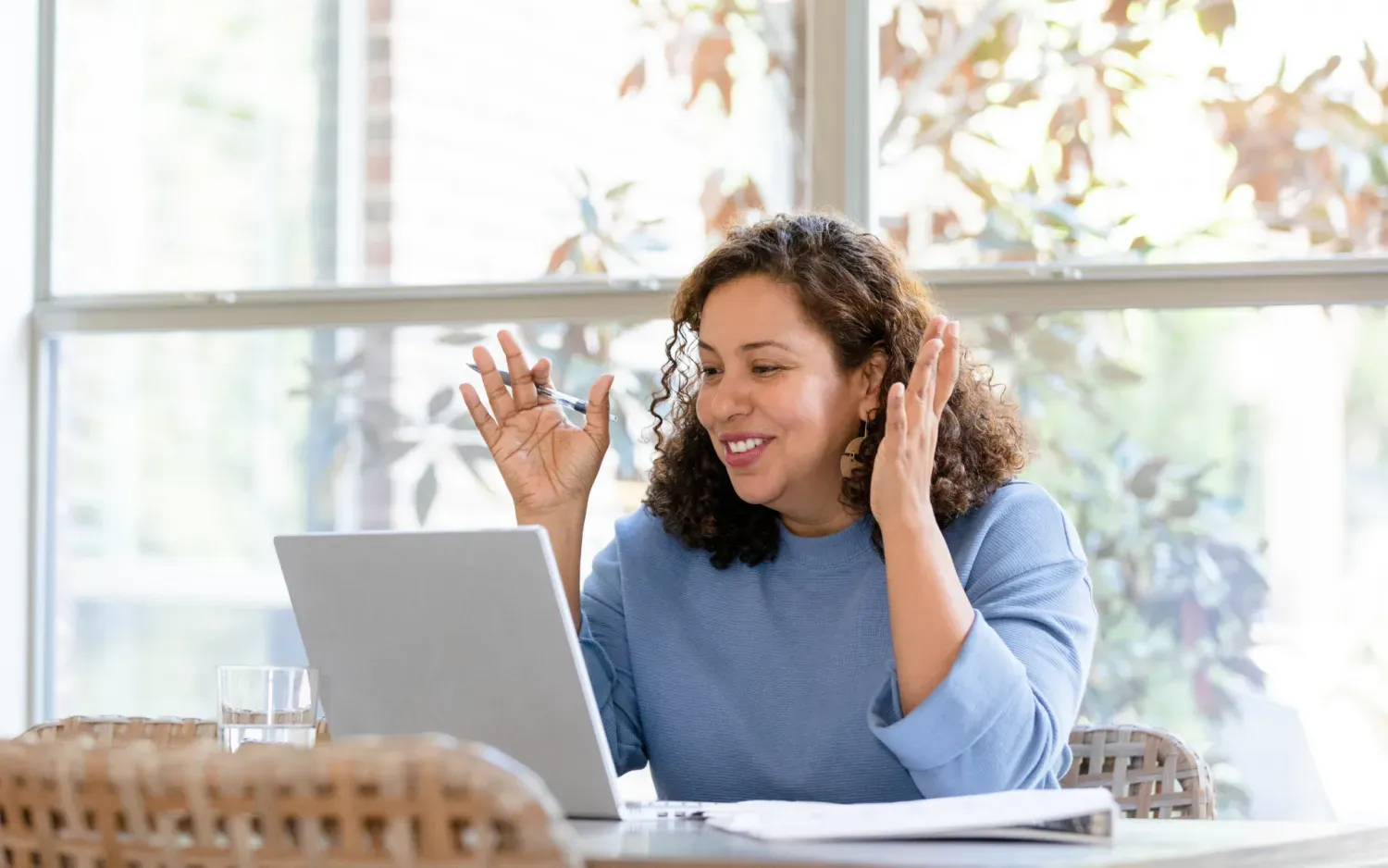 Woman smiling and gesturing during a video call at a laptop in a bright room