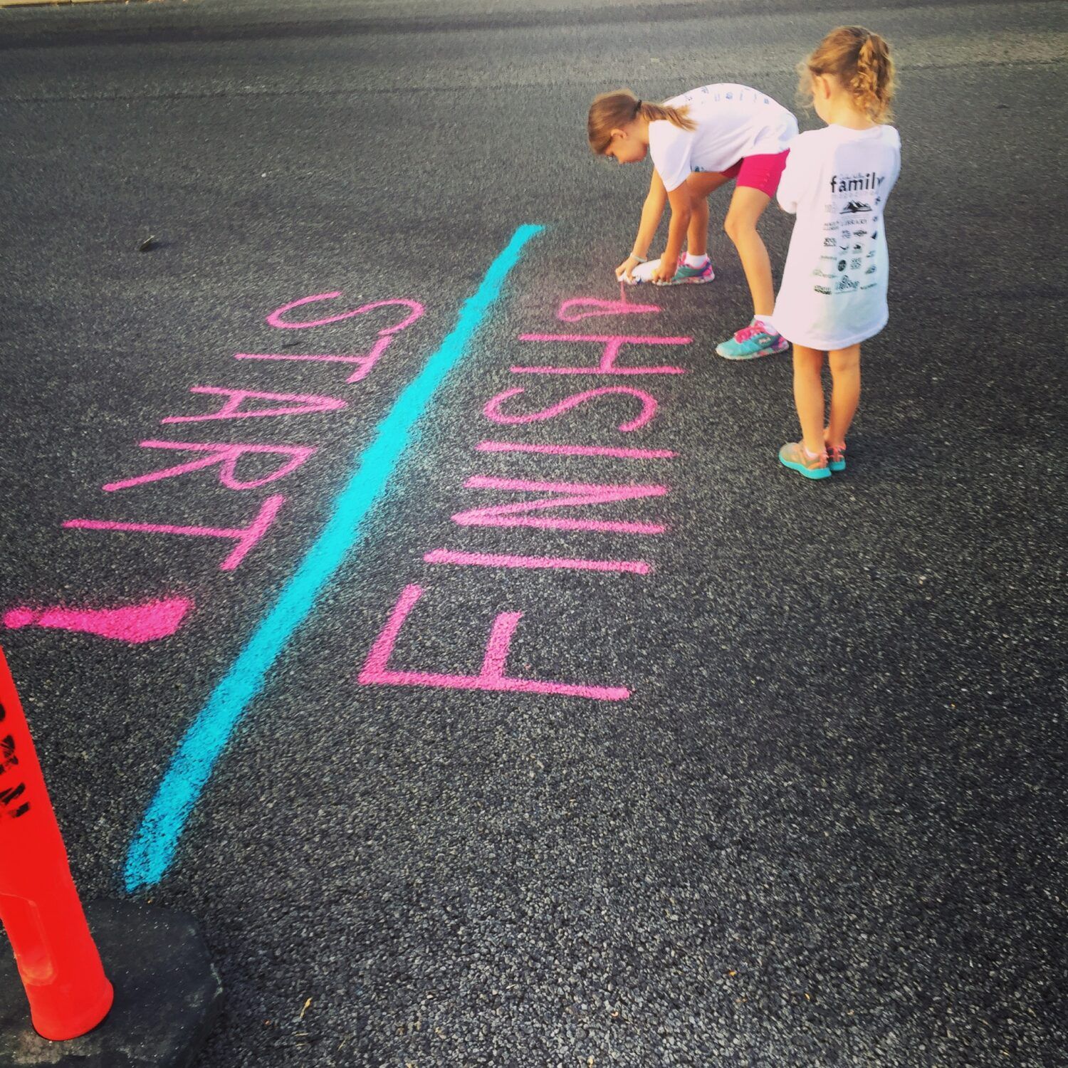 Children at a chalk start-finish line on asphalt, one crouching near the finish.