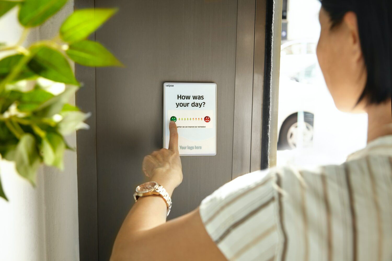 Person pressing a wall-mounted access button beside a doorway, with plants in the foreground.