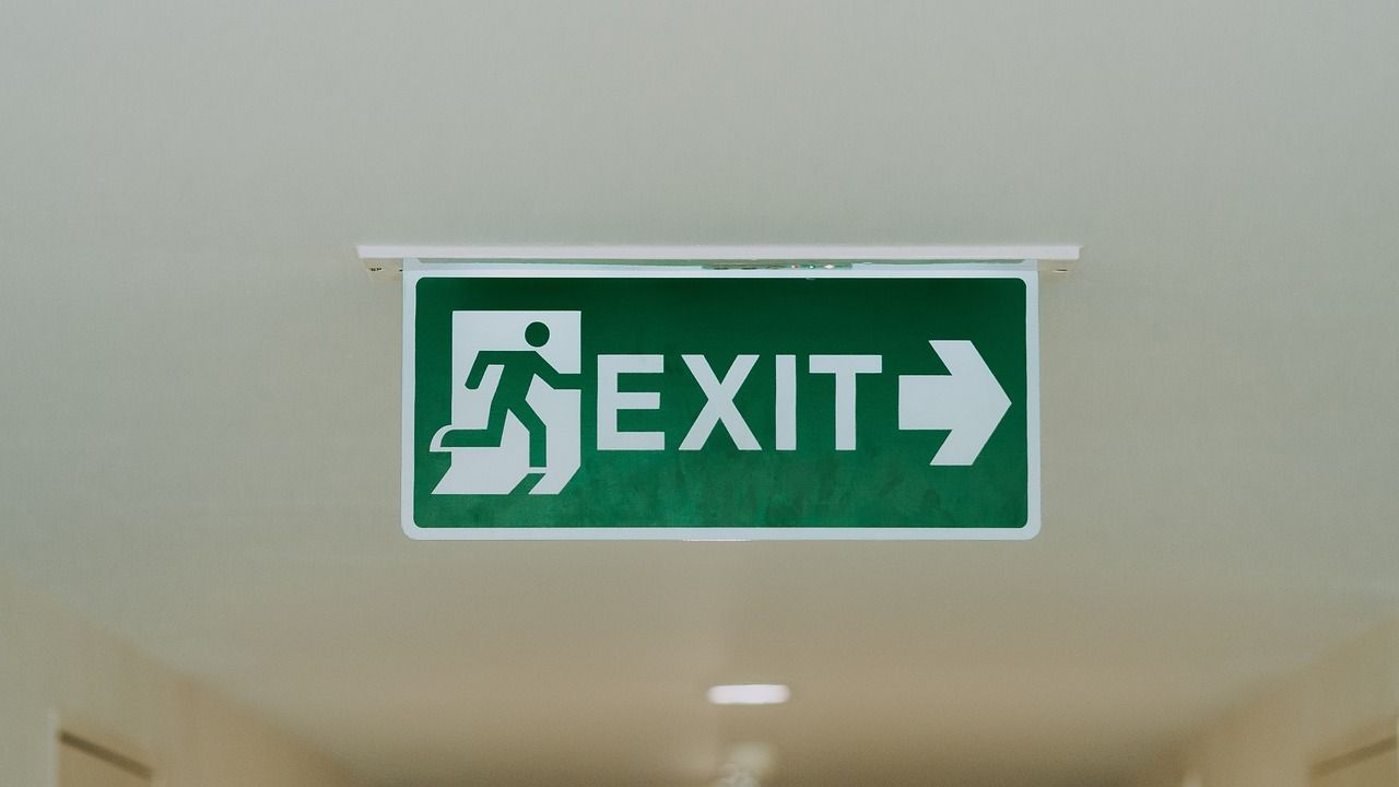 Green EXIT sign with running figure and right arrow hanging indoors on a ceiling.