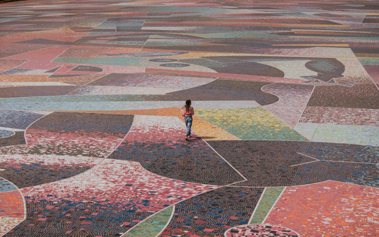 Person standing in a colorful, geometric outdoor plaza pattern