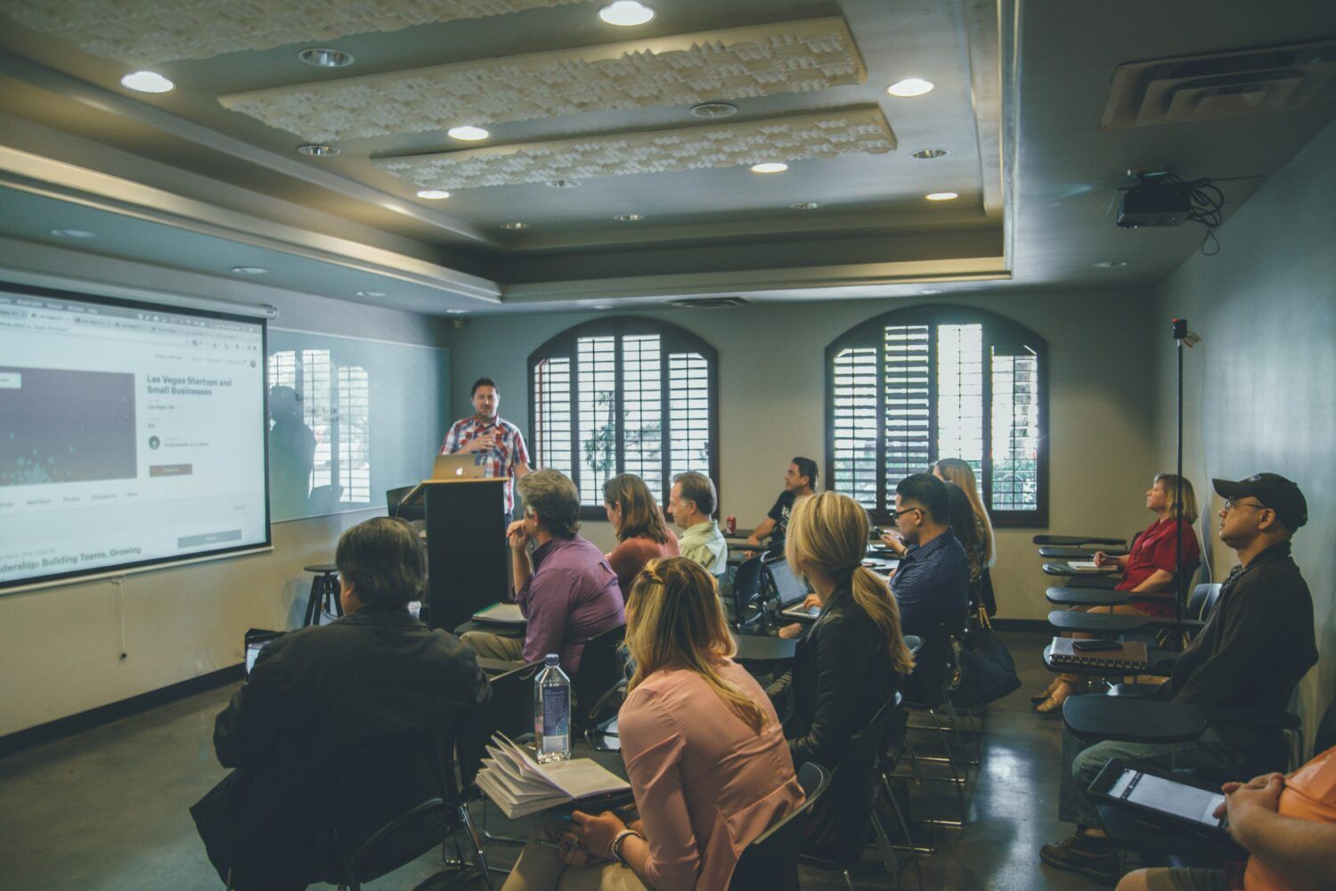 Conference room with people seated for a presentation beside a projected slide and podium