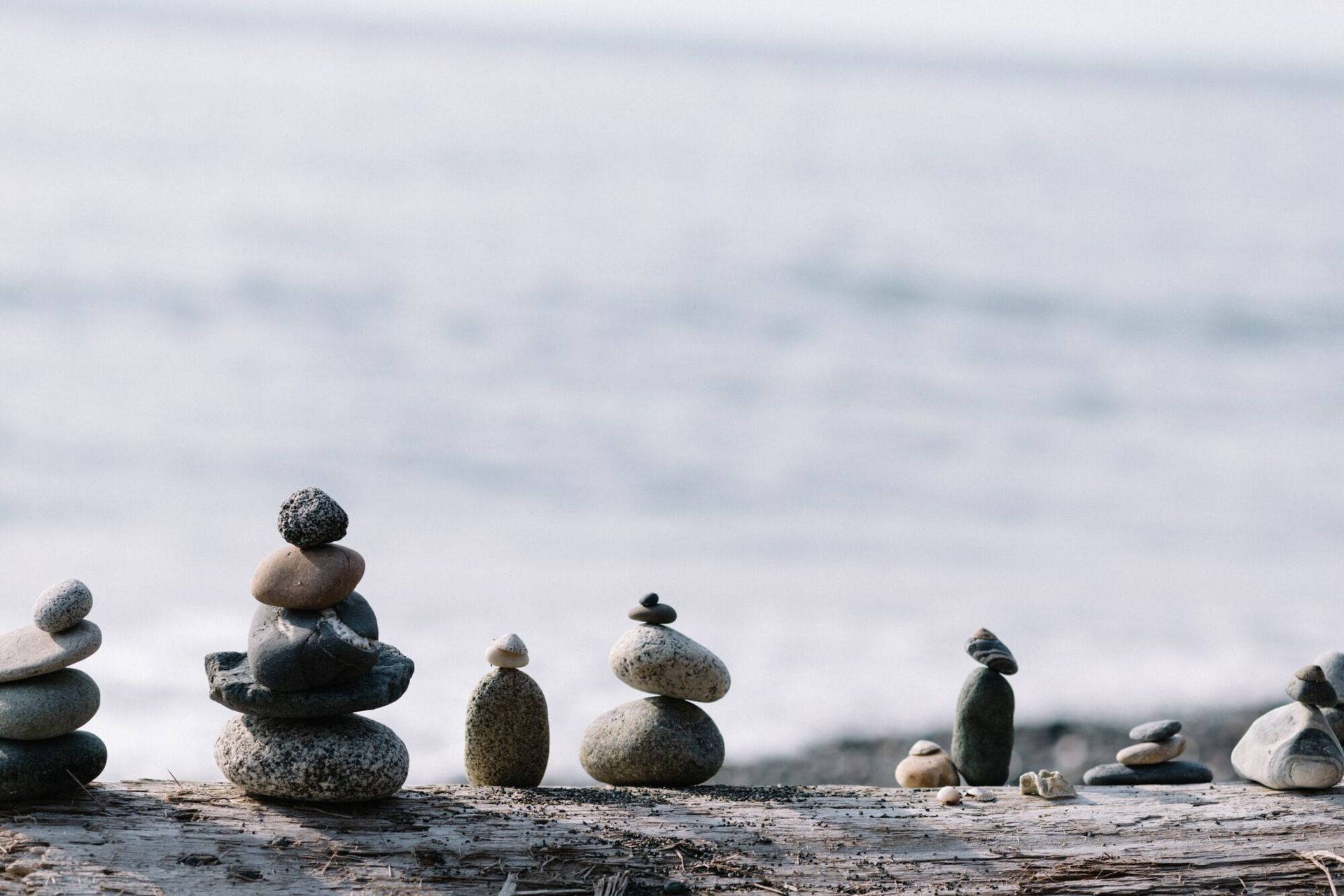 Stacked stones and small pebble towers on a rocky shore beside a calm, blurred sea.