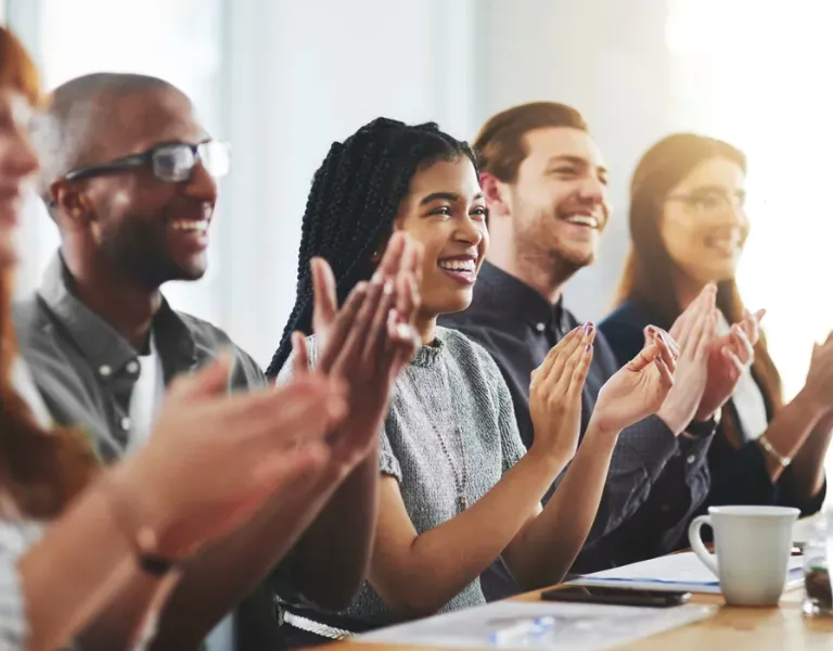 People seated at a conference table applauding and smiling in a bright meeting room