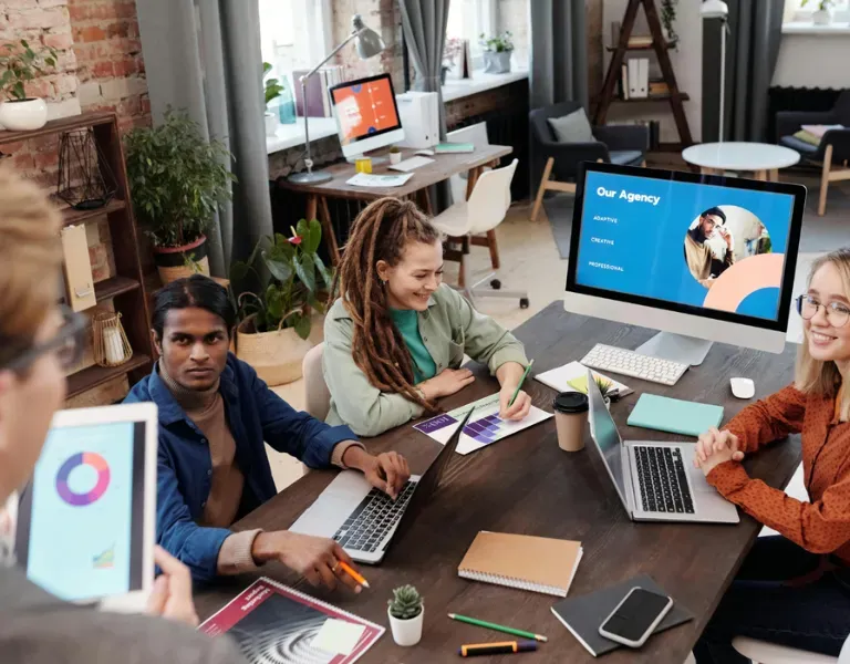Colleagues in a modern office meeting around laptops and a monitor displaying a presentation