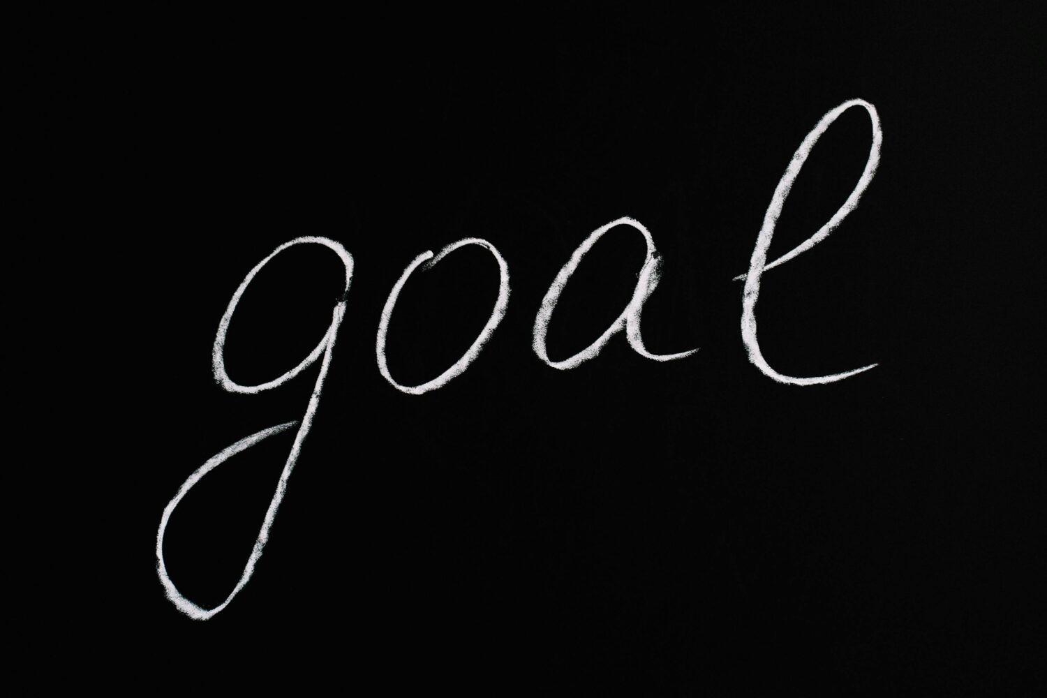 White handwritten word “goal” on a black background.