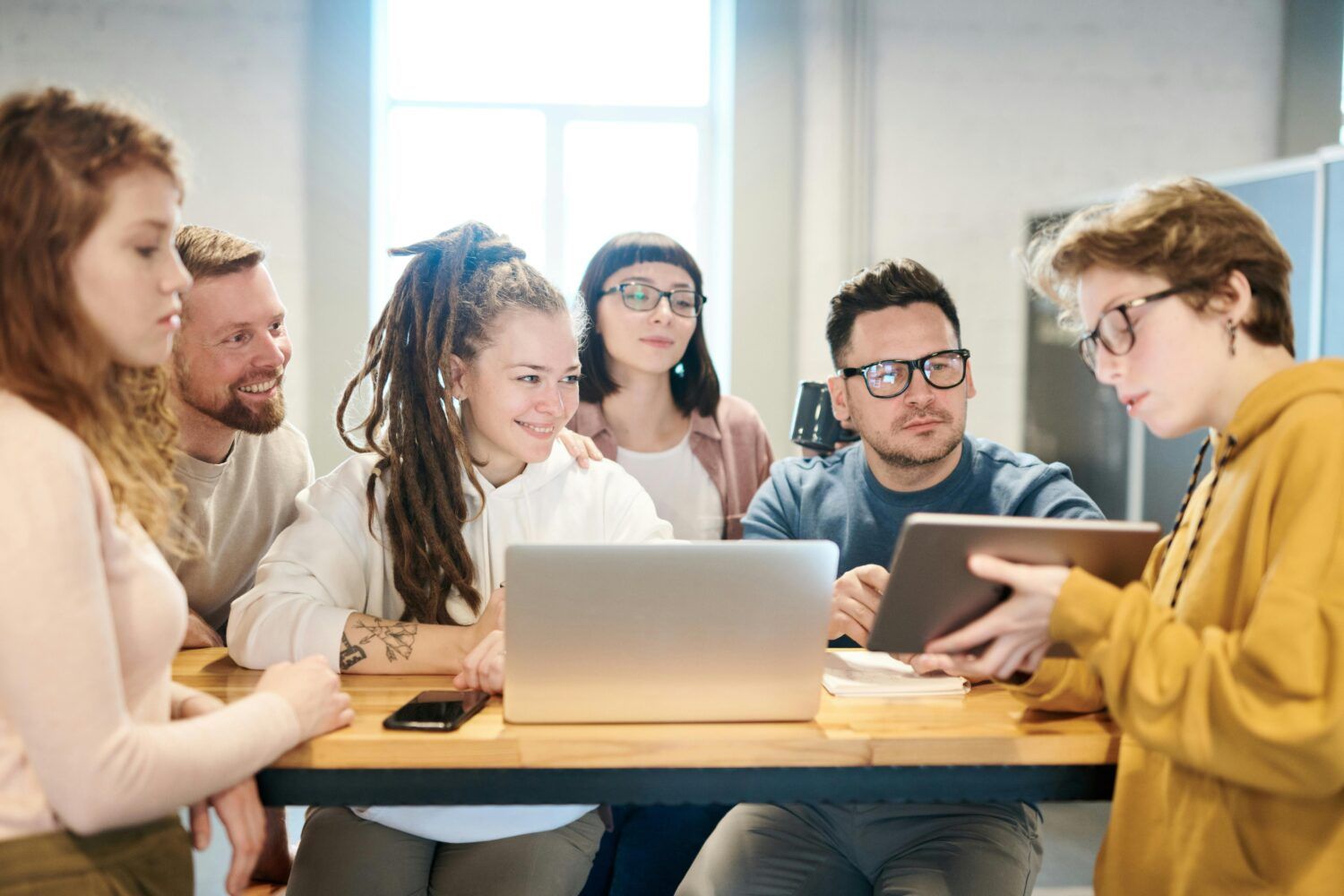 Group collaborating around a laptop and tablet at a table in a bright office
