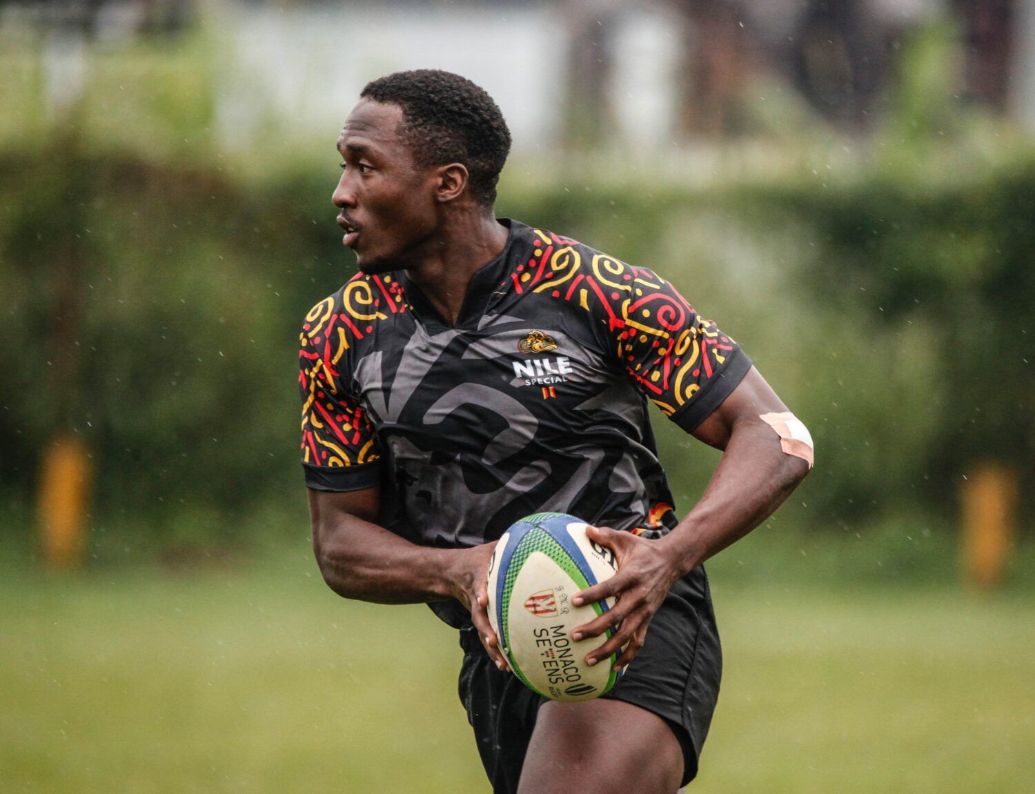 Rugby player in a black patterned jersey running with the ball on a grassy field