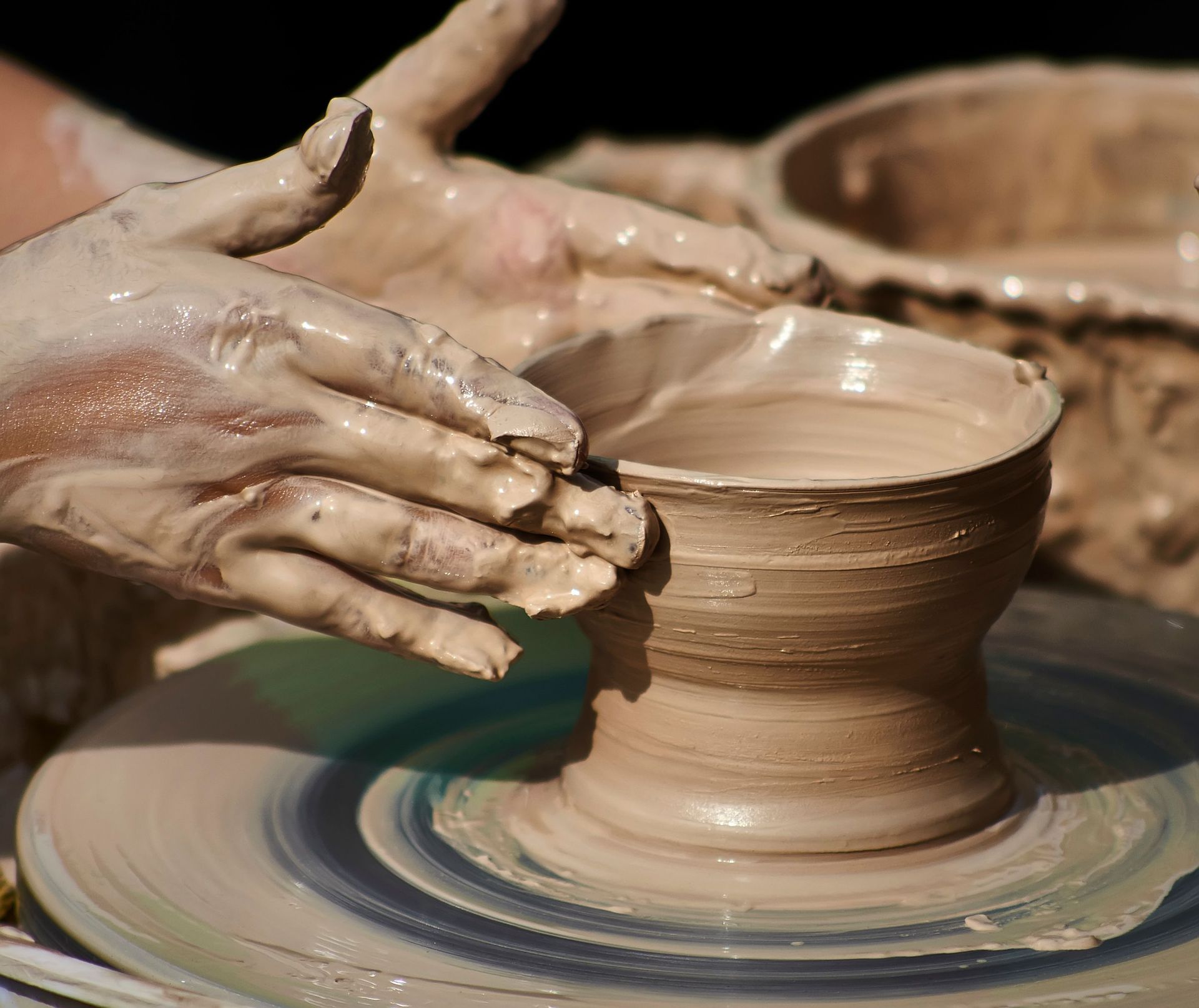 Hands shaping a clay pot on a spinning pottery wheel, with wet clay and a workshop background