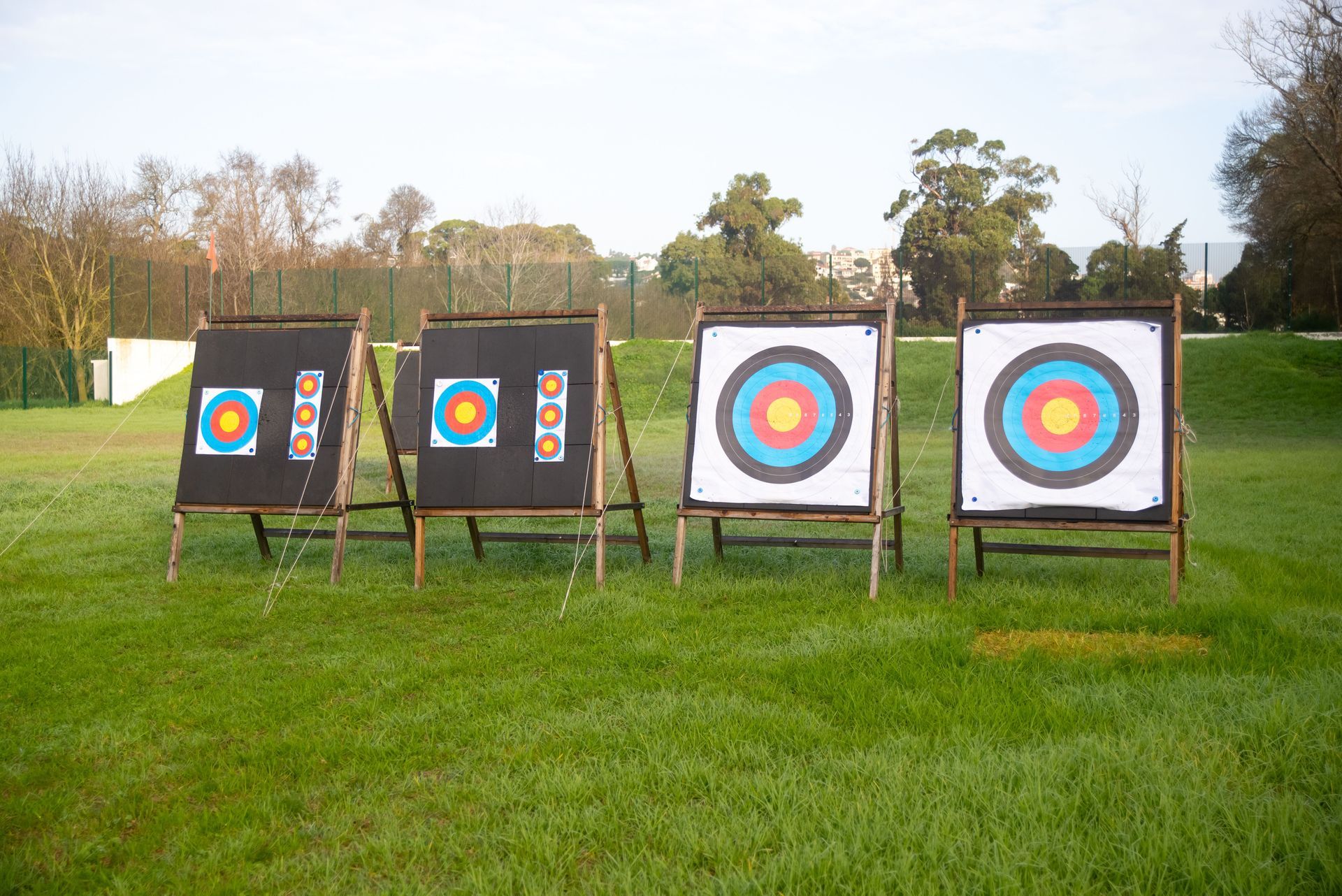 Archery targets on stands in a grassy field, with trees and houses in the background.