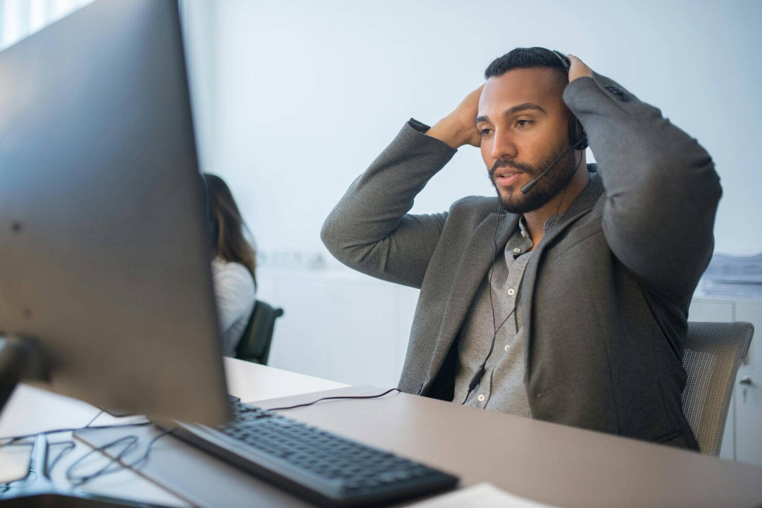 Man seated at desk with hands on head, looking stressed in front of a computer monitor
