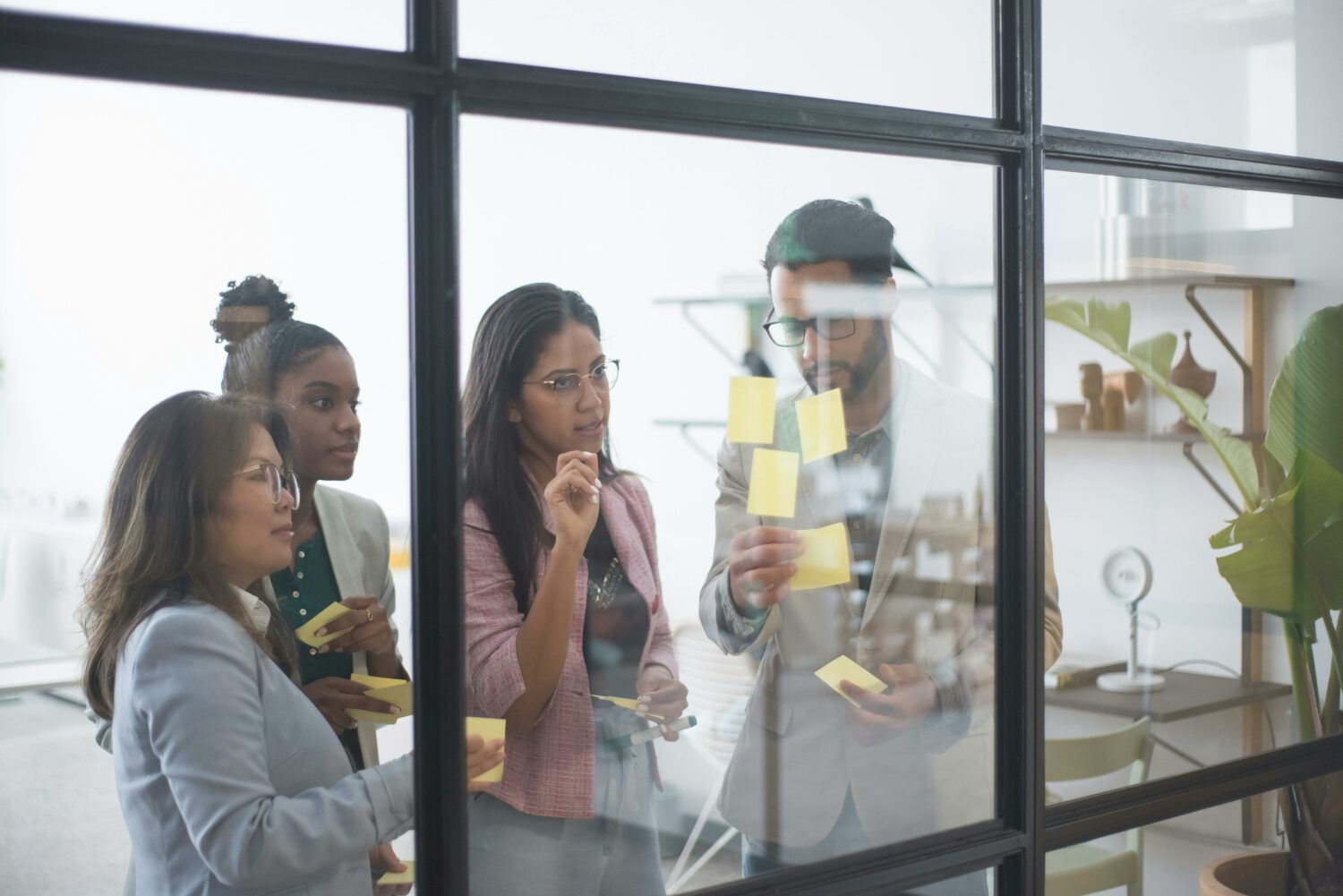 People collaborating with sticky notes on a glass wall in a bright office