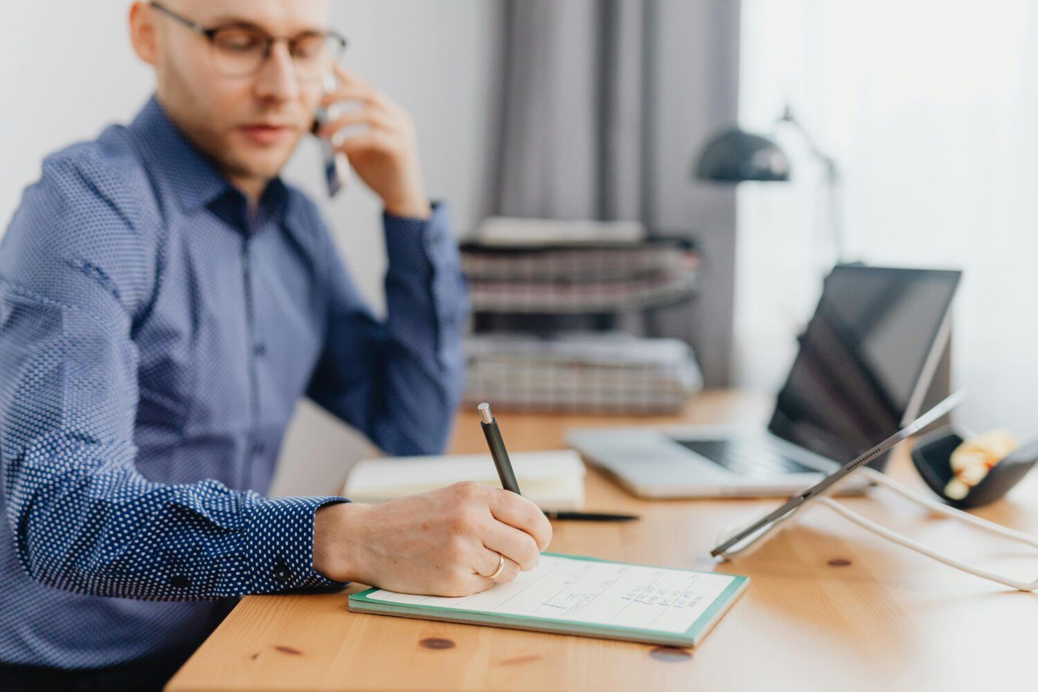 Person writing notes at a desk with a laptop in a bright office