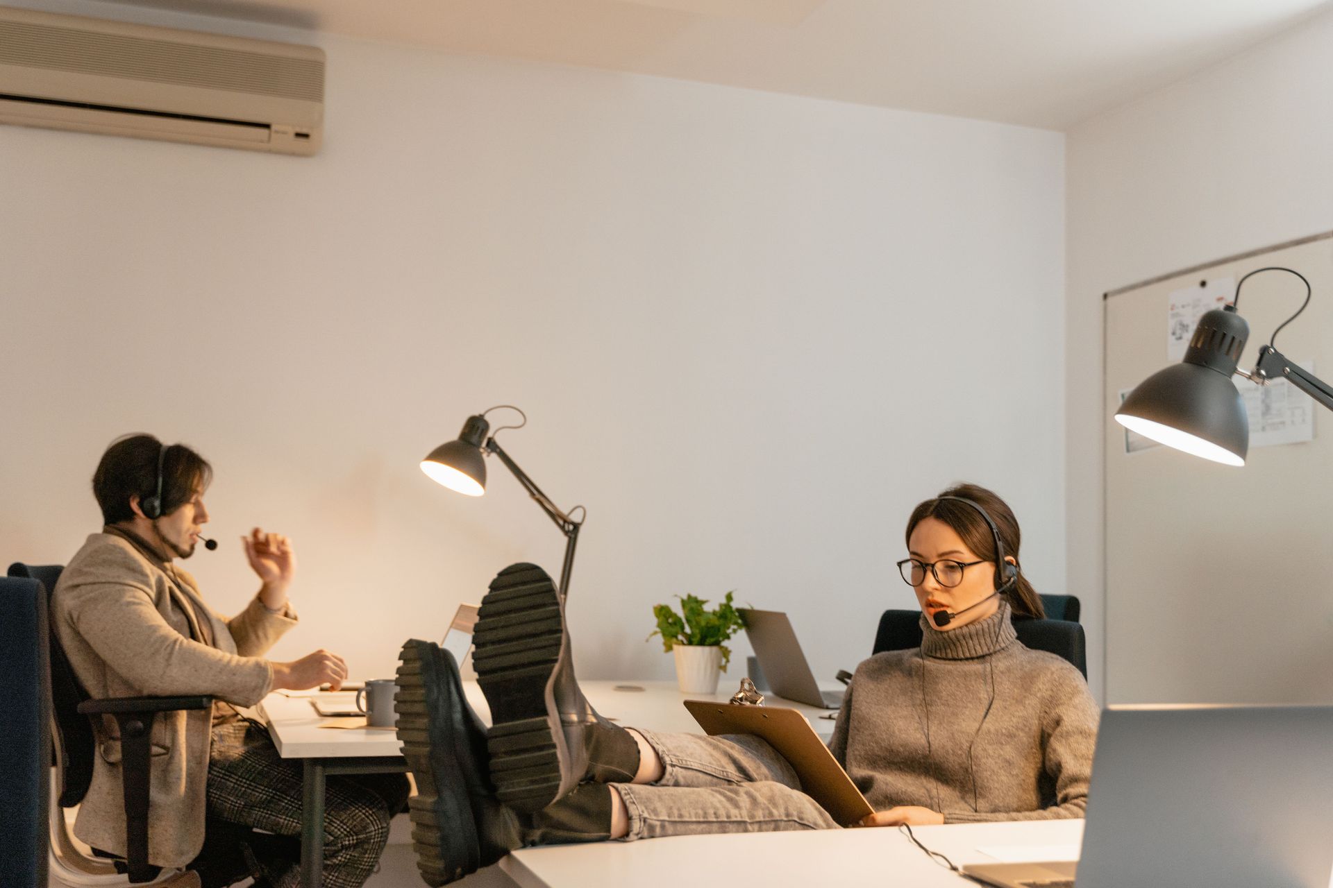 Two people working at desks in a bright office, one using a laptop and the other holding a phone.