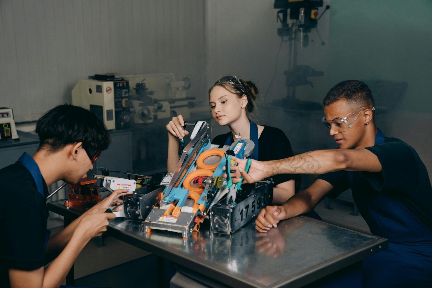 Three people assembling a colorful robot at a table in a workshop-like room