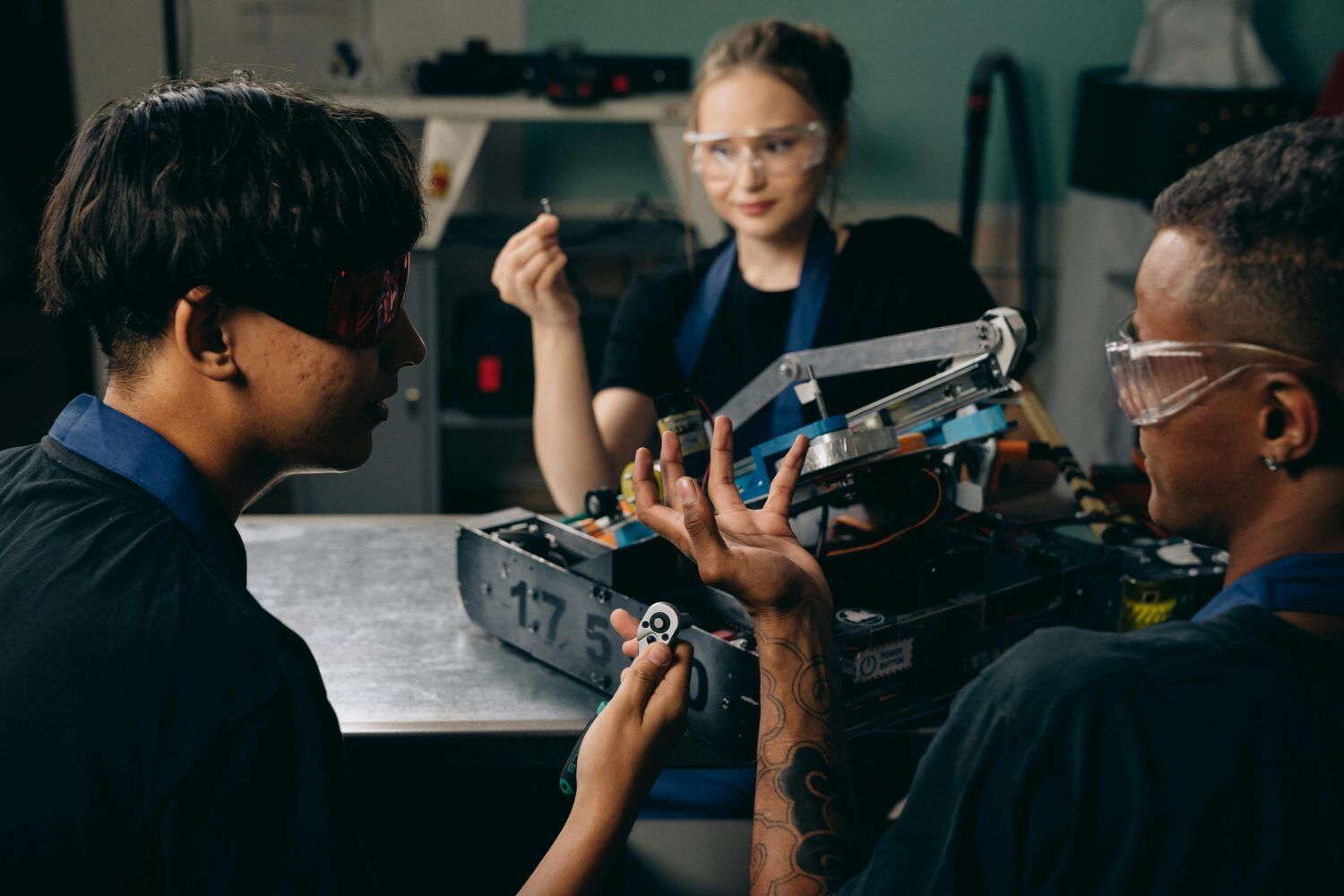 Three students collaborating on a robotics project at a table in a classroom