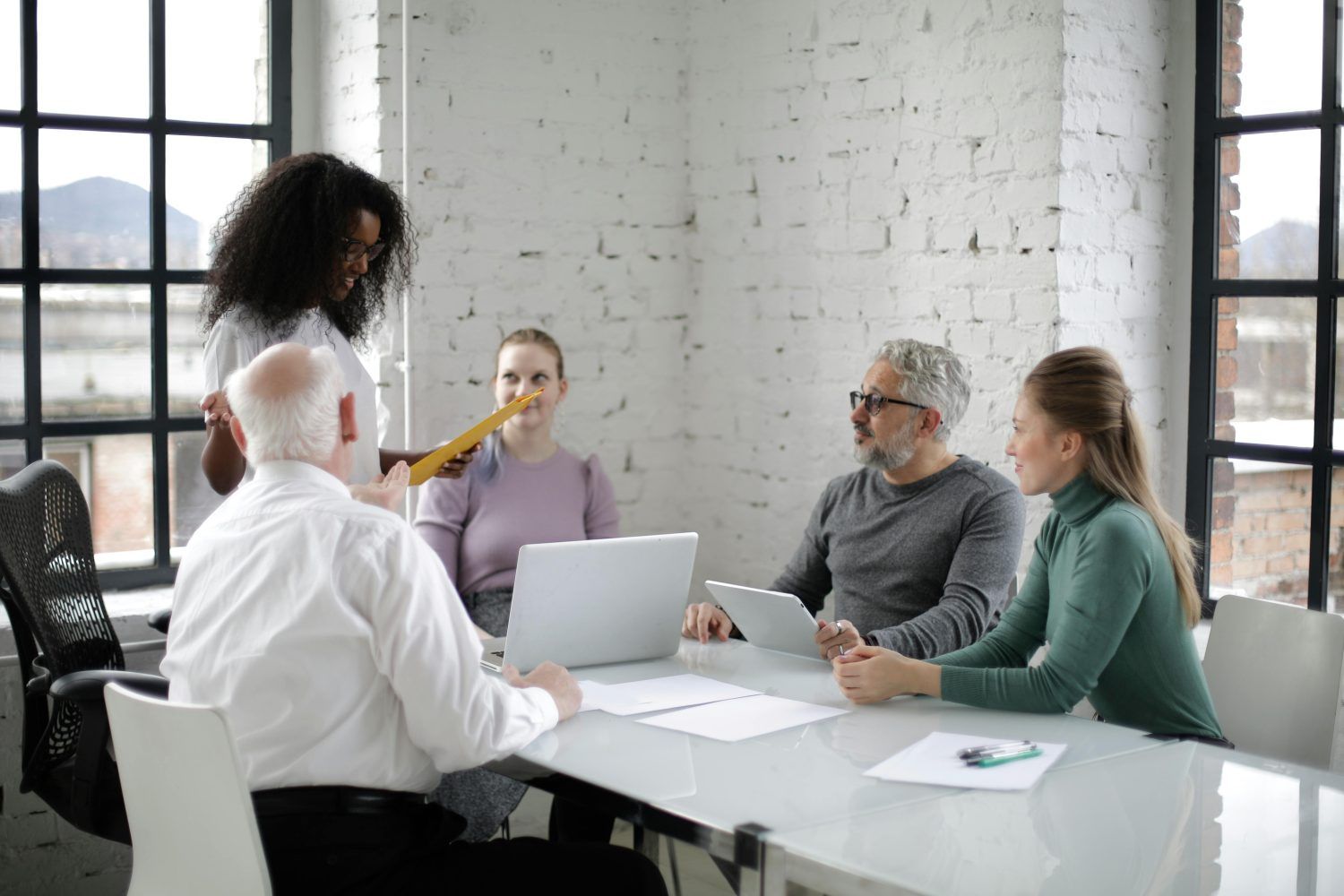 Team meeting in a bright office, with five people gathered around a table and a laptop.
