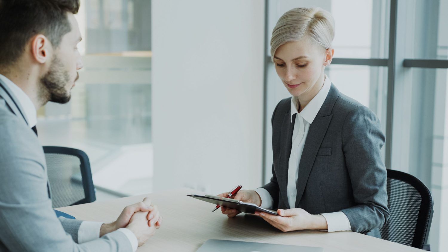Two people in a bright office discuss documents across a table