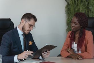 Two people in a meeting reviewing a tablet at a desk, one speaking while the other listens attentively.